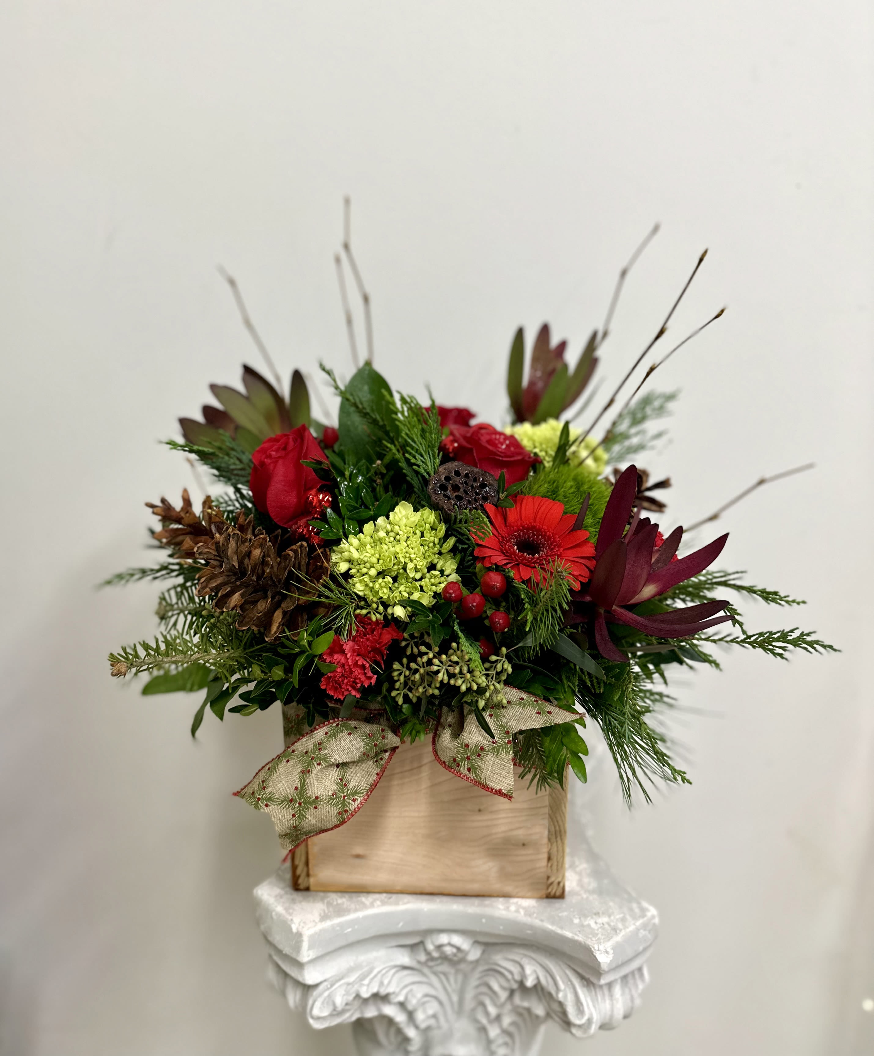 Heritage Kindle by Westford Florist Art by Veny - Elevate your space with the Heritage Kindle by Westford Florist Art by Veny, a stunning arrangement that beautifully captures the essence of nature's bounty. This exquisite centerpiece features a delightful blend of vibrant red and lush green flowers, harmoniously accented with pinecones, safari sunset blooms, berries, and rich evergreens. Each element is thoughtfully nestled in a handcrafted rustic wooden box made from aromatic red cedar, exuding warmth and charm. The elegant ribbon adornment enhances its sophisticated appeal while ensuring it fits seamlessly into any décor. Ideal for gifting or as a striking focal point in your home or office, the Heritage Kindle brings together artistry and natural beauty in one captivating piece. Experience the perfect blend of tradition and elegance—transforming ordinary moments into cherished memories.