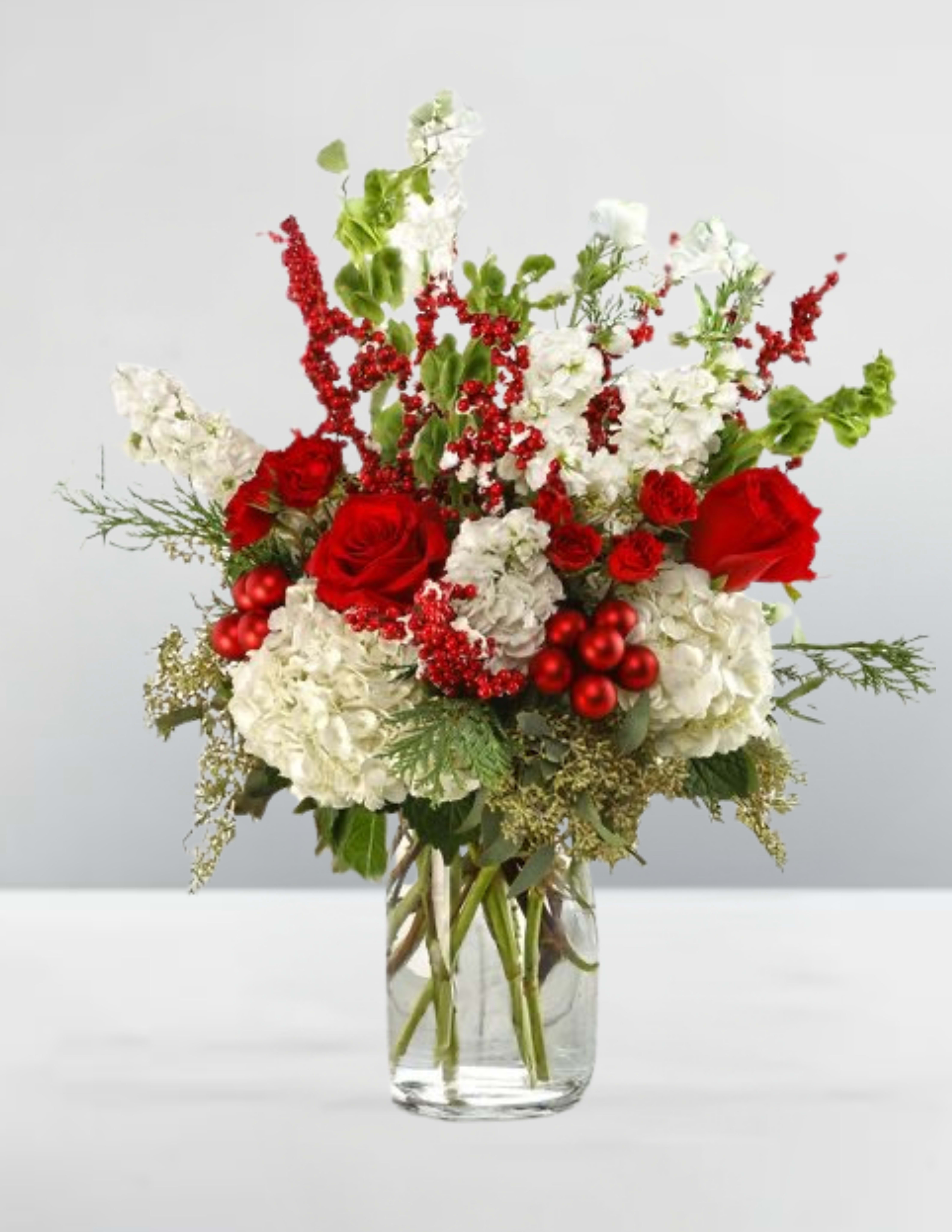 Berry merry -  Berry Merry  Bursting with seasonal joy, Berry Merry blends classic red roses, snowy white hydrangeas, and fragrant stock in a celebration of holiday elegance. Red berries and ornament balls twinkle among lush greenery and bell-shaped blooms, creating a vibrant centerpiece that feels both merry and refined. Designed to dazzle on mantels or tabletops, it’s a floral toast to the most wonderful time of the year.