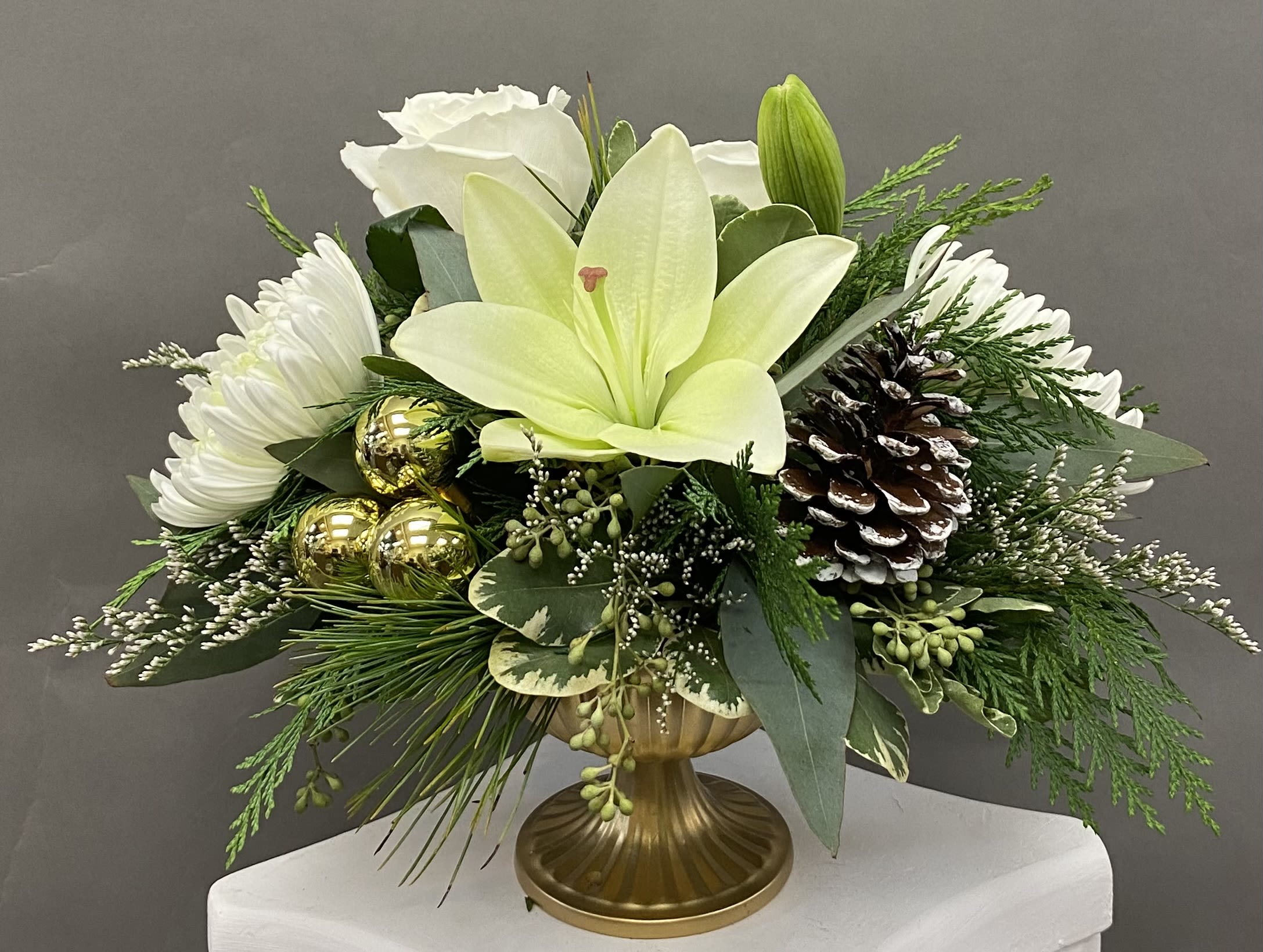 Glamorous Gold  - A petite arrangement  styled for any holiday setting. White lilies &amp; roses are accented with flocked pine cones and gold ornament balls. 
