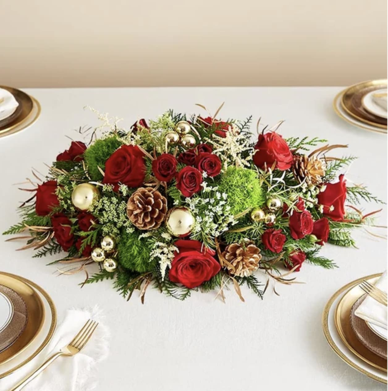 Lavish Christmas Centerpiece - Our lavish centerpiece arrangement creates a dazzling display for a season of celebrating. Beautifully designed with unique white astilbe and festive red Christmas blooms, it’s finished off with gold-tinted greenery and shimmering golden ornaments, adding a touch of glamour to the table for all those holiday gatherings.  Centerpiece arrangement with white astilbe, red roses and spray roses, green dianthus, Queen Anne’s Lace, gold-tinted eucalyptus, assorted Christmas greenery and gold ball ornaments