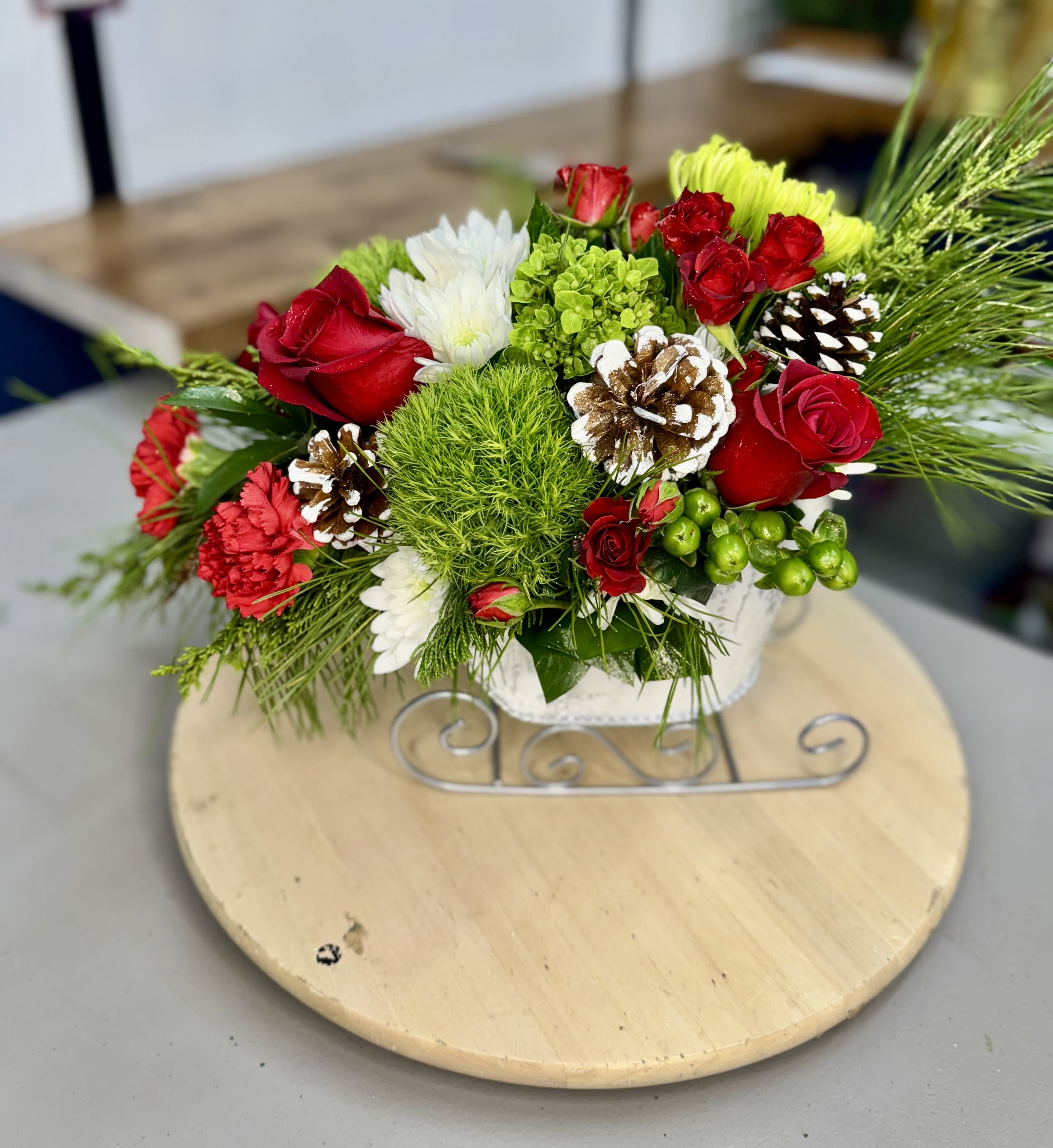 Holiday Sleigh Bloom - This charming holiday arrangement features roses and dianthus in vibrant festive colors, beautifully displayed in a decorative sleigh. Perfect as a gift or to brighten your space this season.