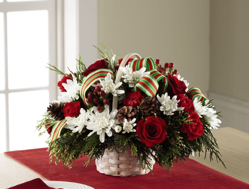  Goodwill &amp; Cheer Basket  - A bright and cheerful Christmas arrangement, this unique basket of blooms can be used throughout the home as a centerpiece, to decorate the buffet, or to simply add a touch of holiday cheer to their favorite room, throughout the holiday season. Rich red roses, red mini carnations, white chrysanthemums, red hypericum berries, and fresh Christmas greens are accented with natural pinecones and a stylish red, green, and white striped grosgrain ribbon while situated in a round white wash woven handled basket. A wonderful way to send your season's greetings this December! 