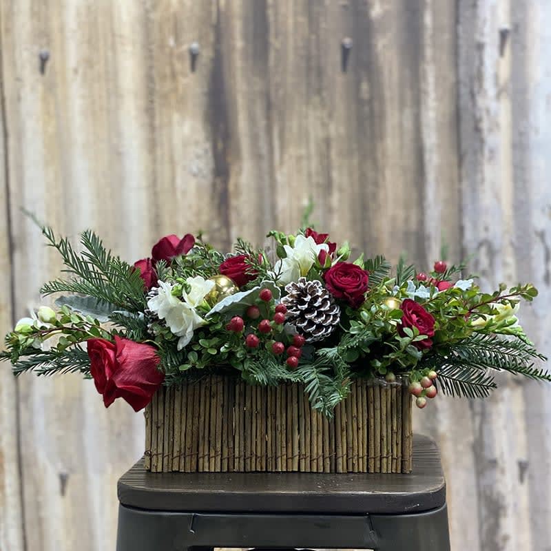 Designer's Choice: Christmas In A Box - An arrangement reminding us of ....  all things Christmas.  Seasonal blooms with Christmas greens. pinecones and ornaments in a designers choice rustic container.  