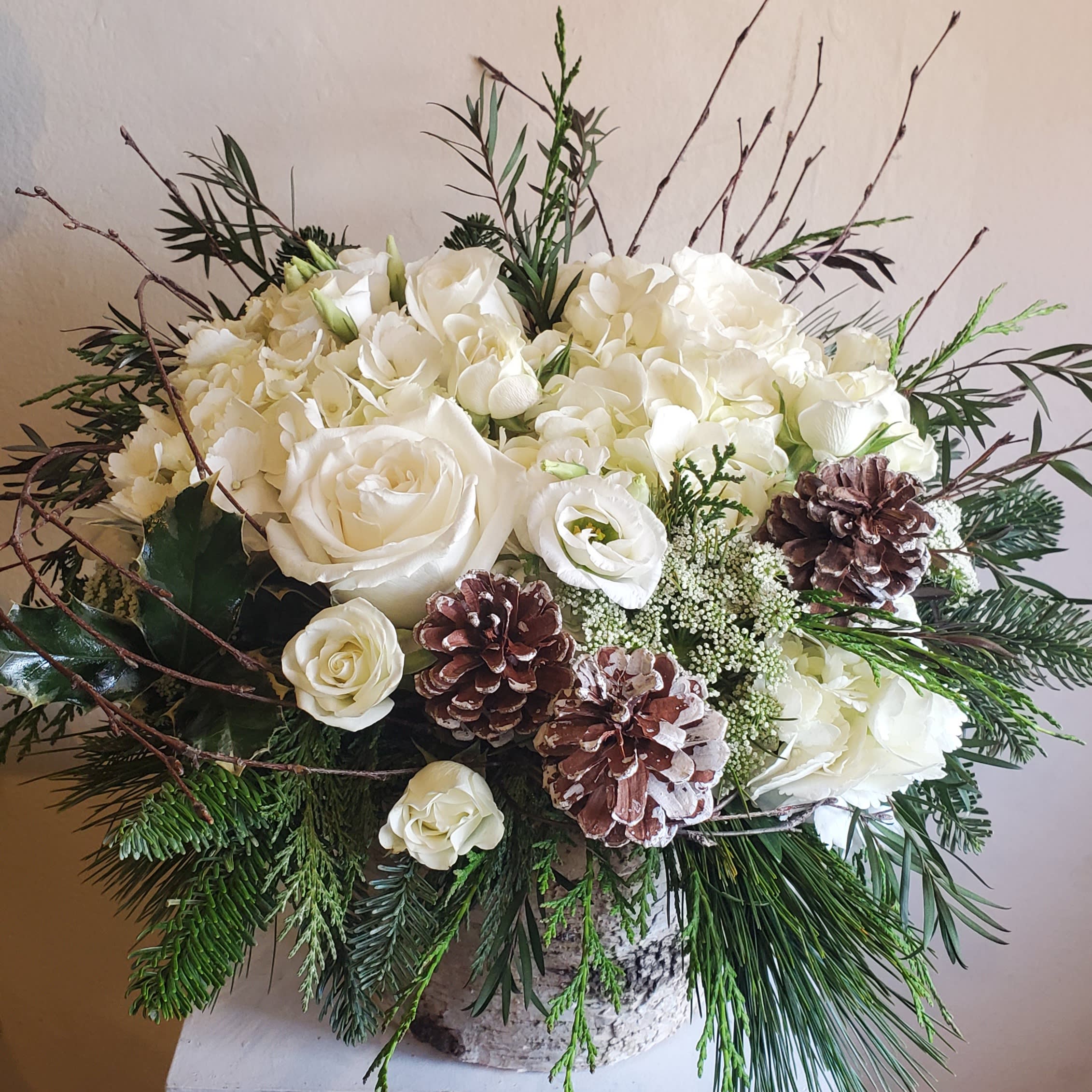 Winter Wonderland - Seasonal white flowers in a birch container with festive pine cones ( please leave a note in special instructions if you would like a touch of red ) Birch container upon availability, substitution will be a glass or ceramic vessel. 