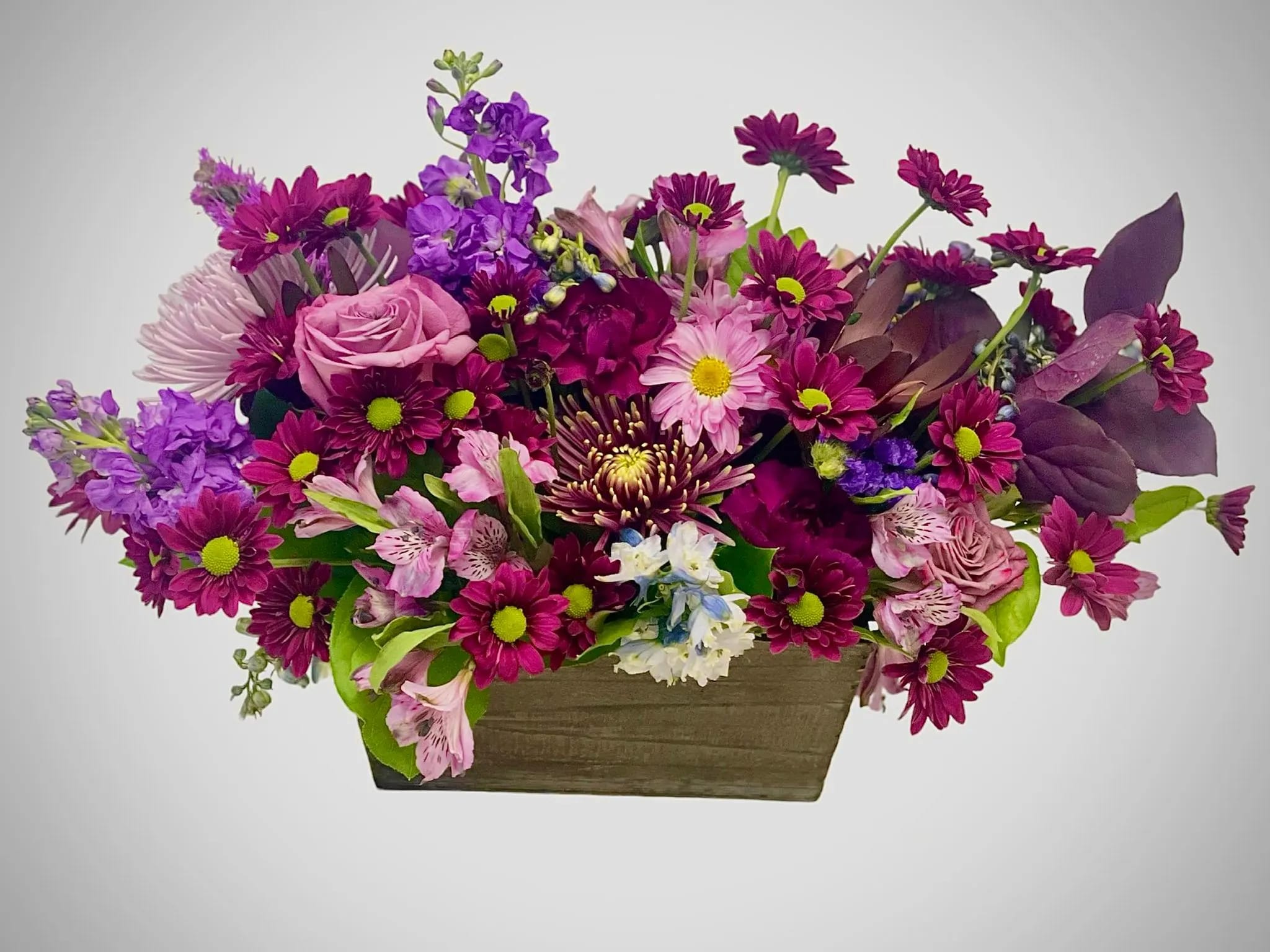  Blossoms of Deep Purple and Plum - Looking for a gift that conveys warmth and sophistication? This arrangement isn't just about color; it's also a celebration of textures. The velvety petals of the deep purple flowers contrast beautifully with the delicate plum accents in a grey-bluish wood box, creating a dynamic interplay that's both soothing and eye-catching.