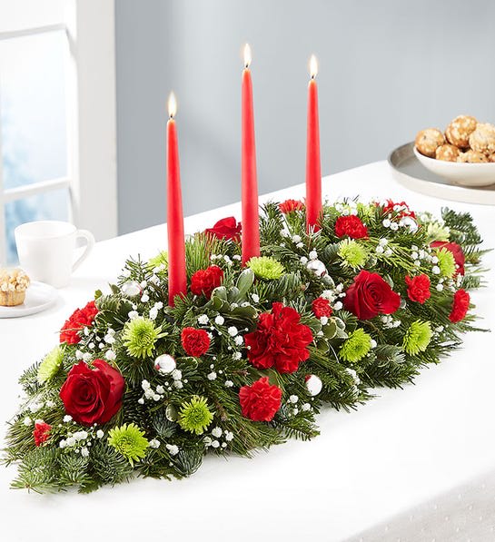 Season's Greetings™ Centerpiece - Send season’s greetings in classic style. Our charming Christmas centerpiece is hand-arranged with red &amp; green blooms and decorated with delightful ornaments. Tapered candles add to the elegance of this traditional design, sure to bring holiday joy into the hearts and homes of family and friends.  Centerpiece arrangement with red roses, carnations and mini carnations; green Athos poms; accented with baby’s breath, assorted Christmas greenery and silver decorative balls