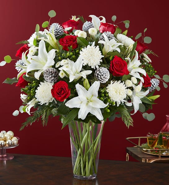 Garden of Grandeur® Holiday - The signature colors of Christmas are on display in our grand holiday arrangement. Loosely gathered with an abundance of red &amp; white blooms, lush greenery and glistening, snow-tipped pinecones, it’s the perfect gift for celebrating the season in luxurious style.  All-around arrangement with red roses; white Oriental lilies, football mums and button poms; accented with green hypericum berries, assorted Christmas greenery and glittery, snowy pinecones
