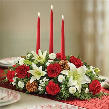 CHRISTMAS CENTERPIECE ARCE - Every family has its own holiday traditions. Let us help you add one more with our classic Christmas centerpiece. Beautifully arranged using fresh blooms in the signature colors of the seasonwhite lilies, red roses and morethis lively display is accented with a fragrant mix of evergreens and pinecones. And for a finishing touch, our florists add a red taper candle, creating a warm and festive glow for all your celebrations!  Hand-crafted arrangement of roses, lilies, carnations, cushion poms and assorted Christmas greens, accented with holly, pinecones and 12&quot;H red taper candles  Large arrangement features 2 candles and measures approximately 7&quot;H x 15&quot;L  Medium arrangement features 1 candle and measures approximately 7&quot;H x 13&quot;L  Small arrangement features 1 candle and measures approximately 7&quot;H x 11&quot;L; arrangement does not include roses, lilies or holly  Dimensions do not include candles  Our florists hand-design each arrangement, so colors, varieties and container may vary due to local availability