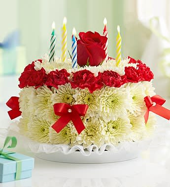 Birthday Flower Cake Bright - Product ID: 1990  Our signature floral birthday cake may look good enough to eat, but it's actually crafted from fresh flowers such as mini carnations and poms. It arrives in a bakery box with a set of candles where available, and with proper care, can last days after the celebration is complete. Fresh, hand-crafted cake-shaped arrangement of bright mini carnations and cushion poms in floral foam, topped with a single bright-colored rose Includes a cake skirt, candles and a bakery box where available Arrangement measures approximately 7&quot;H x 8&quot;D Our florists hand-design each arrangement, so colors, varieties, and container may vary due to local availability