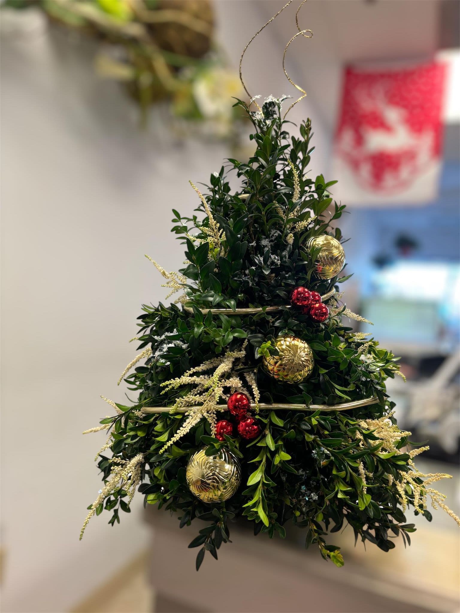 Evergreen Elegance Tree - Add a timeless touch of holiday elegance to your home or office with our handcrafted Boxwood Christmas Tree! This arrangement is perfect for spreading seasonal cheer, made with fresh boxwood greenery and adorned with shimmering gold ornaments, festive red berries, and delicate decorative accents. FRESH FLOWERS CAN BE ADDED PER YOUR REQUEST.