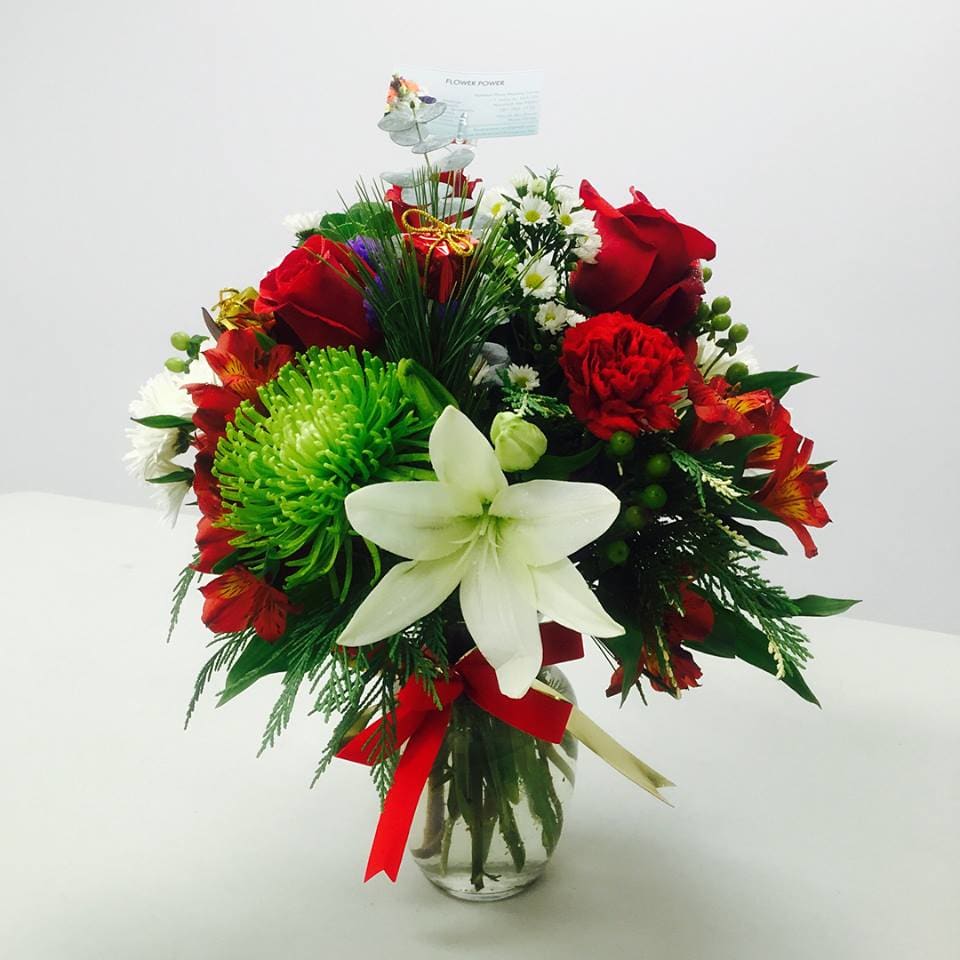 Traditional Christmas - A bouquet of red, white, and green fresh flowers with Christmas greens  in a clear glass vase,and a ribbon on neck.