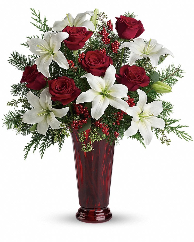 Holiday Magic - With beautiful red roses and brilliant white lilies delivered in a dramatic tall ruby vase, this dazzling holiday arrangement casts an enchanting spell. A step up from the traditional, its effect is nothing less than magical. White asiatic lilies, red roses, fir, cedar and eucalyptus create the perfect holiday bouquet, especially when delivered in a stunning ruby red roman column vase.