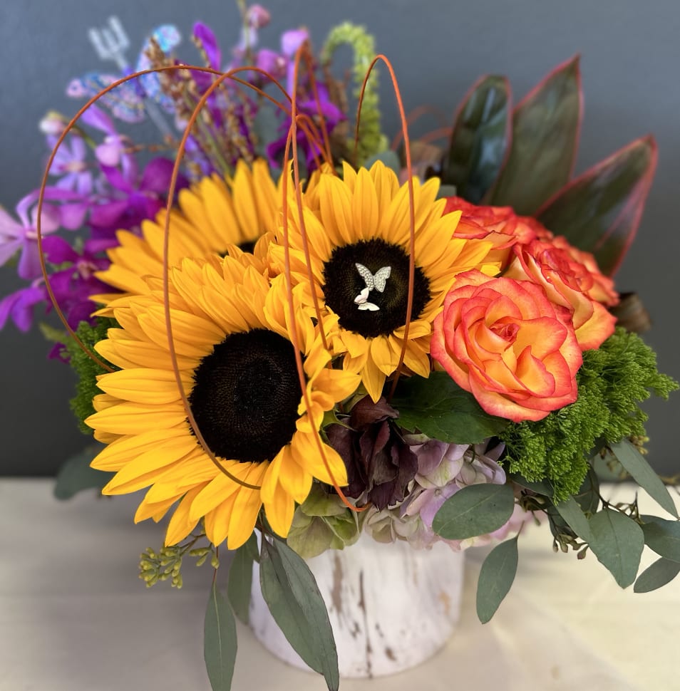 Autumn Trio - Sunflowers, Orchids, Roses  - Sunflowers, Orchids, and Roses are uniquely designed in a ceramic vase with accented tropical leaves and assorted foliage. 