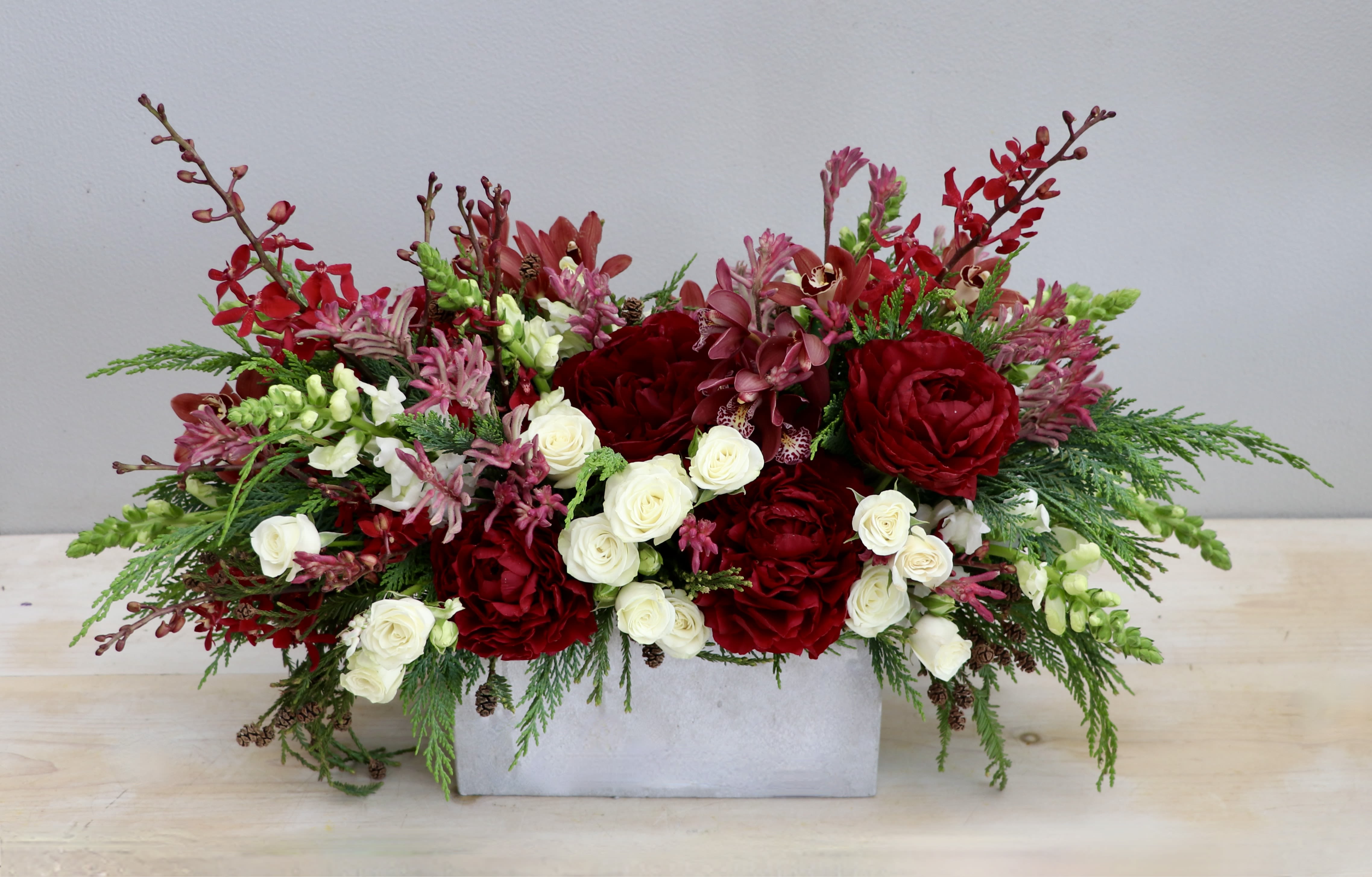 Peonies &amp; Pine - My Glendale Florist - This lovely arrangement is made with lush red peonies and orchids and accented with fragrant seasonal greens. White spray roses and snapdragons give this arrangement pops of light in the dark winter. 