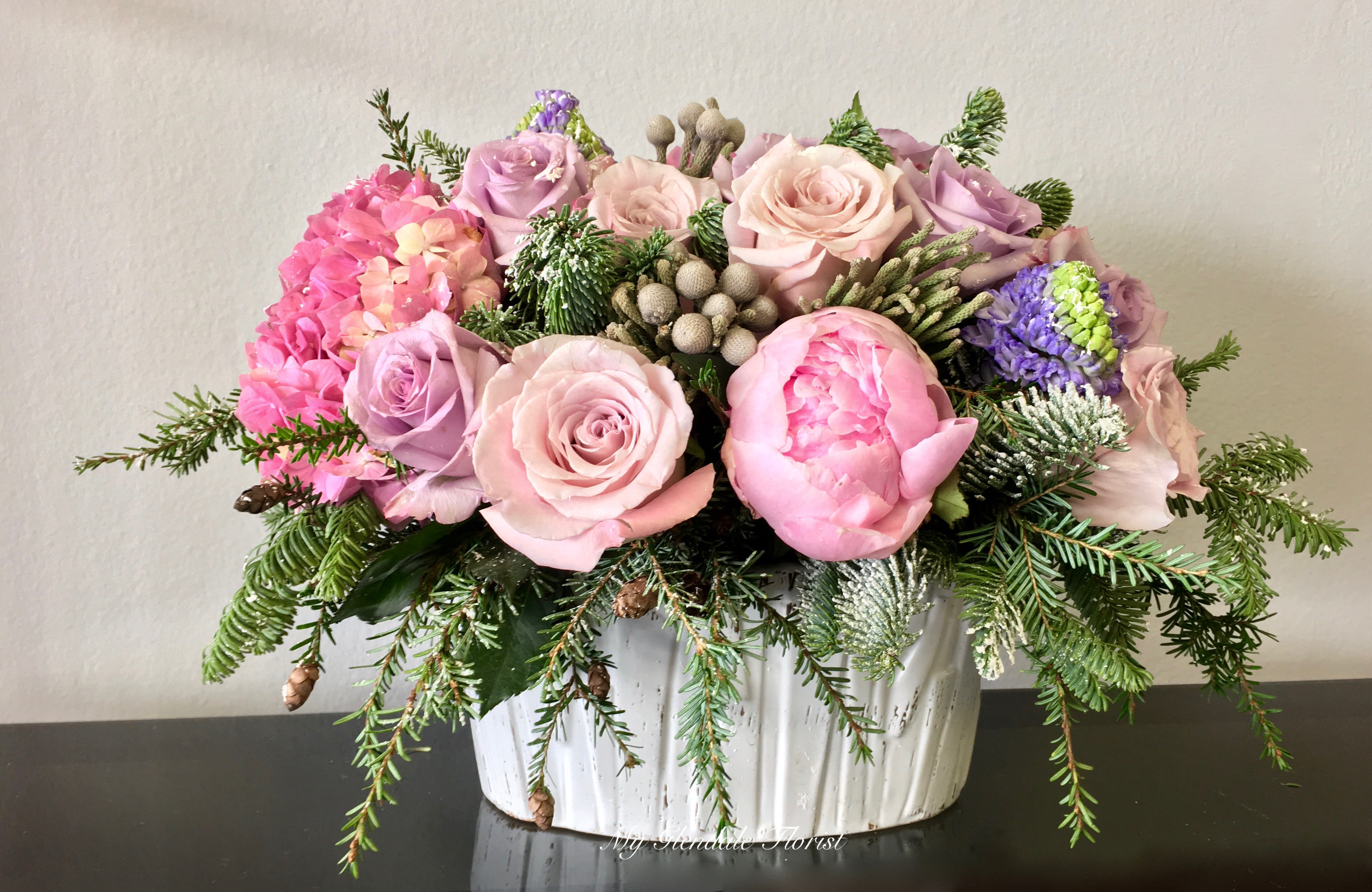 Pastel Holiday - Glendale Florist - 'Tis the season to soften up the colors. A touch of fir to add to the holiday spirit and you have an arrangement that will be remembered for holidays to come. Once the holidays are over the vase can be saved for future decor. Standing approximately 12'' and 14'' wide.