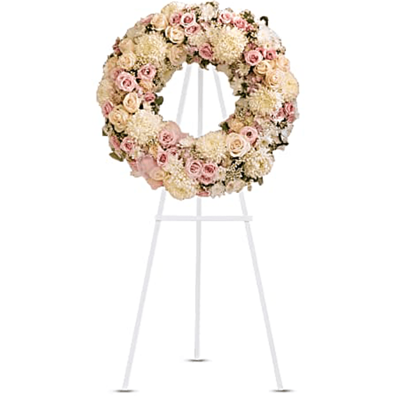 The Peace Eternal Wreath Standing Spray - A pure and delicate expression of adoration. Accented with a sheer pink organza bow, this wreath of white, crème, and pale pink petals gently embraces loving memories, and offers solace and sweet thoughts at a time of loss. Lovely blooms such as crème and pink roses, pink hydrangea and white chrysanthemums are nestled together and accented with organza ribbon. A touching and feminine wreath, ideal for a memorial service. Orientation: One-Sided