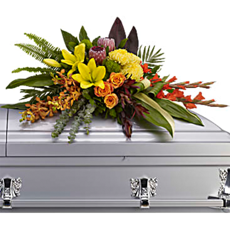 The Island Memories Half Casket Cover - Tropical flowers evoke tropical breezes in this modern style casket spray. Deep red ti leaves and aspidistra leaves frame fresh and fragrant yellow lilies and chrysanthemums, along with orange orchids, roses and red gladioli. Casket spray includes flowers such as orange orchids and roses, red gladioli and pink ice protea, plus yellow asiatic lilies and chrysanthemums, accented by red ti leaves, aspidistra leaves, sword fern and eucalyptus.