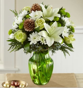 Holiday Bliss Bouquet - A winter wonderland that blossoms with an elegant holiday style, this fresh flower bouquet is set to delight your special recipient with each beautiful bloom. Crisp white Asiatic Lilies and chrysanthemums look snowy and bright amongst jade green roses, bright green button poms, gold pine cones, and an assortment of fragrant Christmas greens arranged beautifully in an eye-catching green swirled glass vase. A wonderful way to send your warmest season's greetings to your recipient this year!