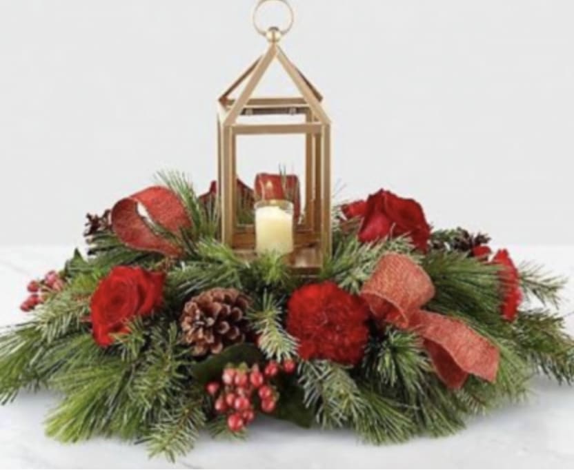 I'll be home for Christmas - Hurricane lantern centerpiece. This brushed gold lantern is a keepsake to treasure. Includes a small votive candle. Full of pine greens and cedar. Standard size include red carnations and berries. Deluxe and Premium sizes will have roses and carnations. 