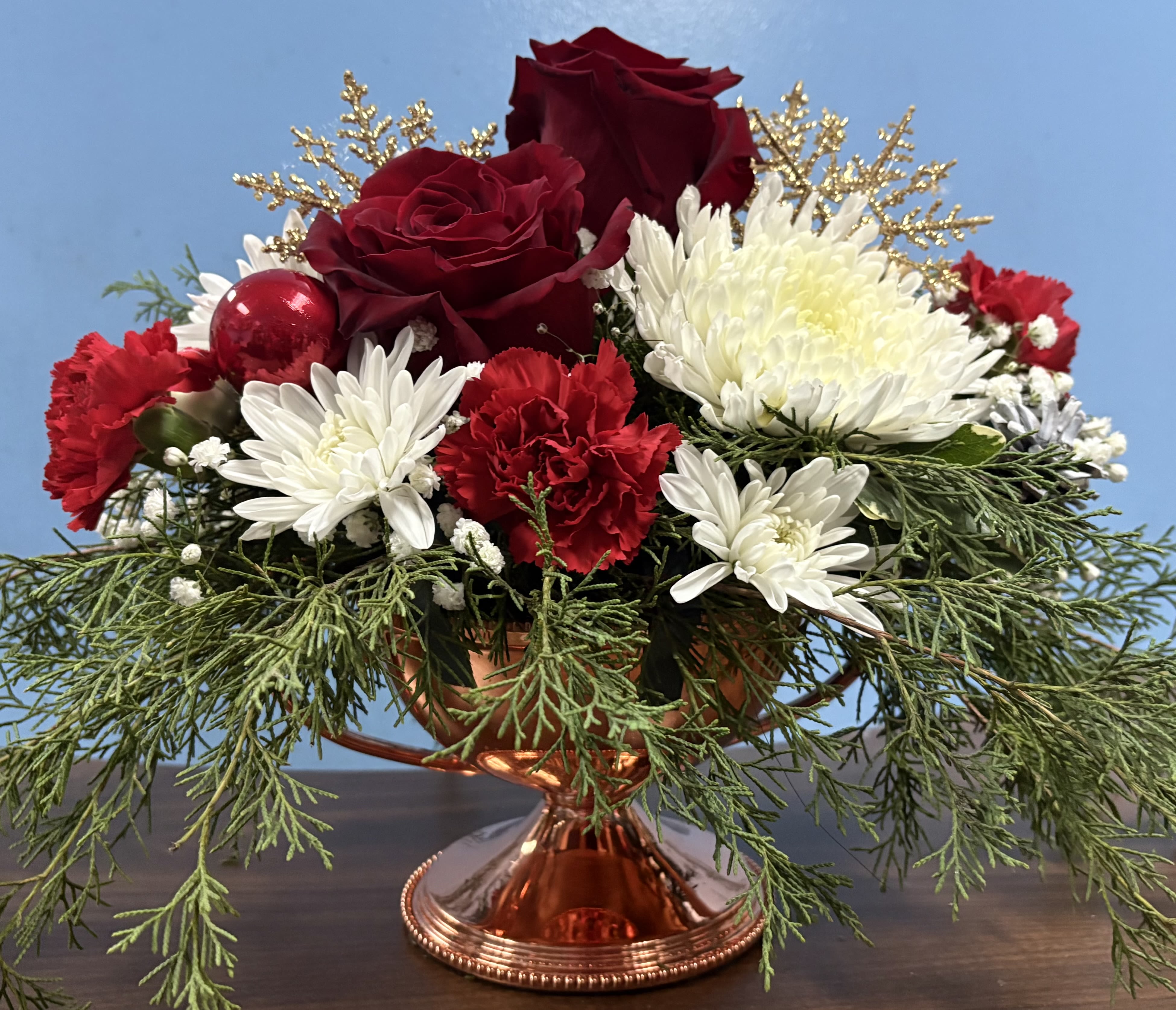 Sassy Brassy Christmas - Our Sassy Brassy Christmas arrangement would be the perfect gift to someone to bring in the holiday cheer. Made in a pedestal brass container designed with roses, poms, carnations and Christmas Greens accented with ornaments.