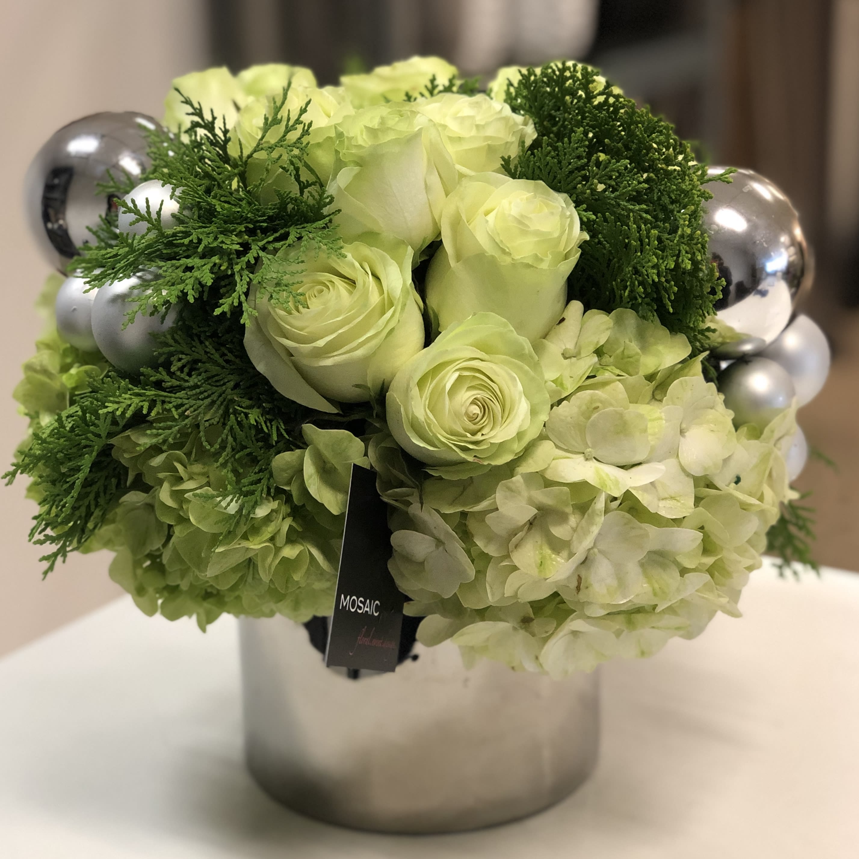 Christmas Gift - Light green roses, light green hydrangeas accented with Christmas silver and frosted ornaments and greens in a 5"x 5" container.  Overall arrangement height is 10" x 10"