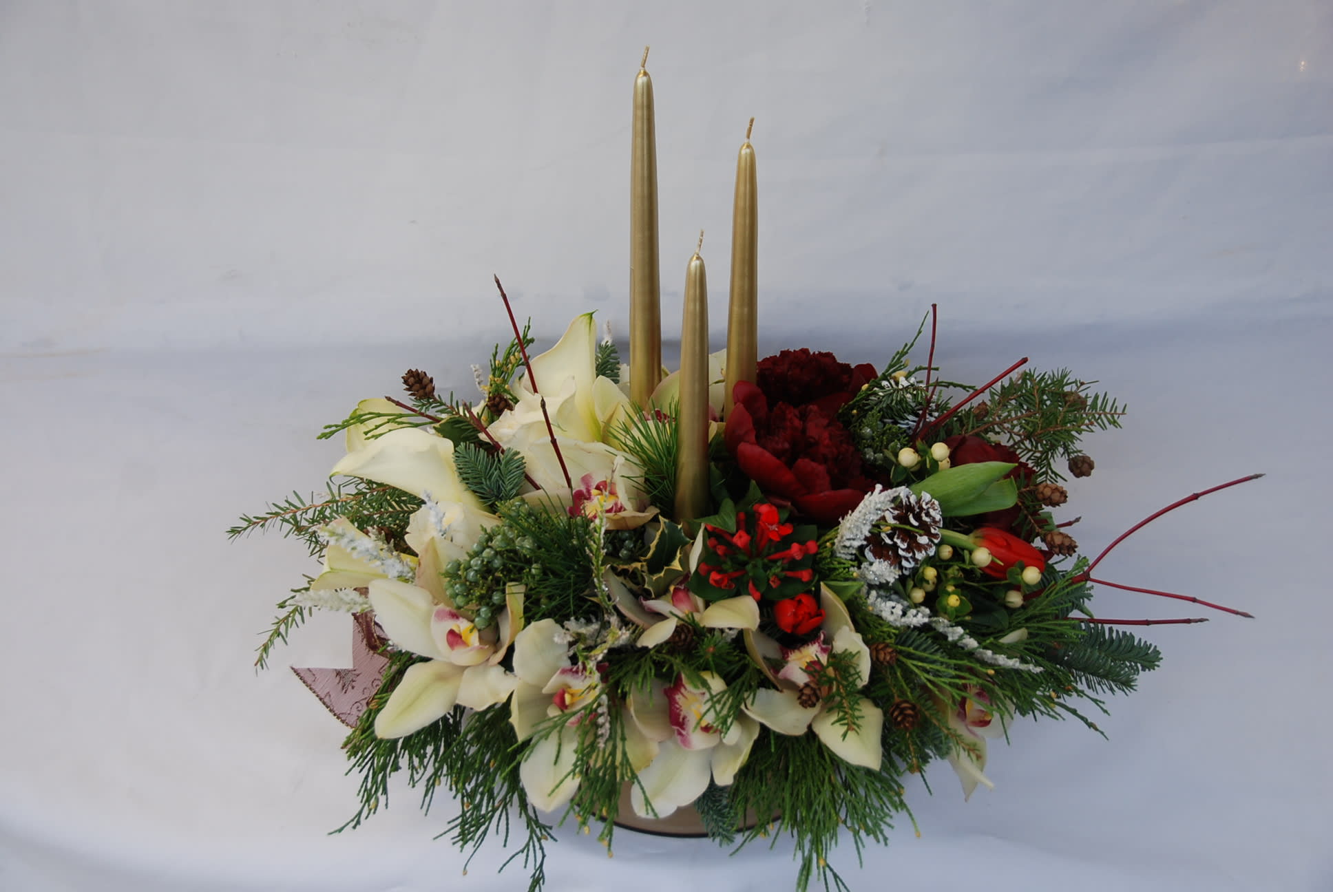 Golden Elegance  - Beautiful evergreens with cymbidium orchids, burgundy peonies, calla lilies, white roses, tulips, bouvardia hypericum berries, and gold candles in a beautiful gold base Christmas Arrangements Centerpieces.