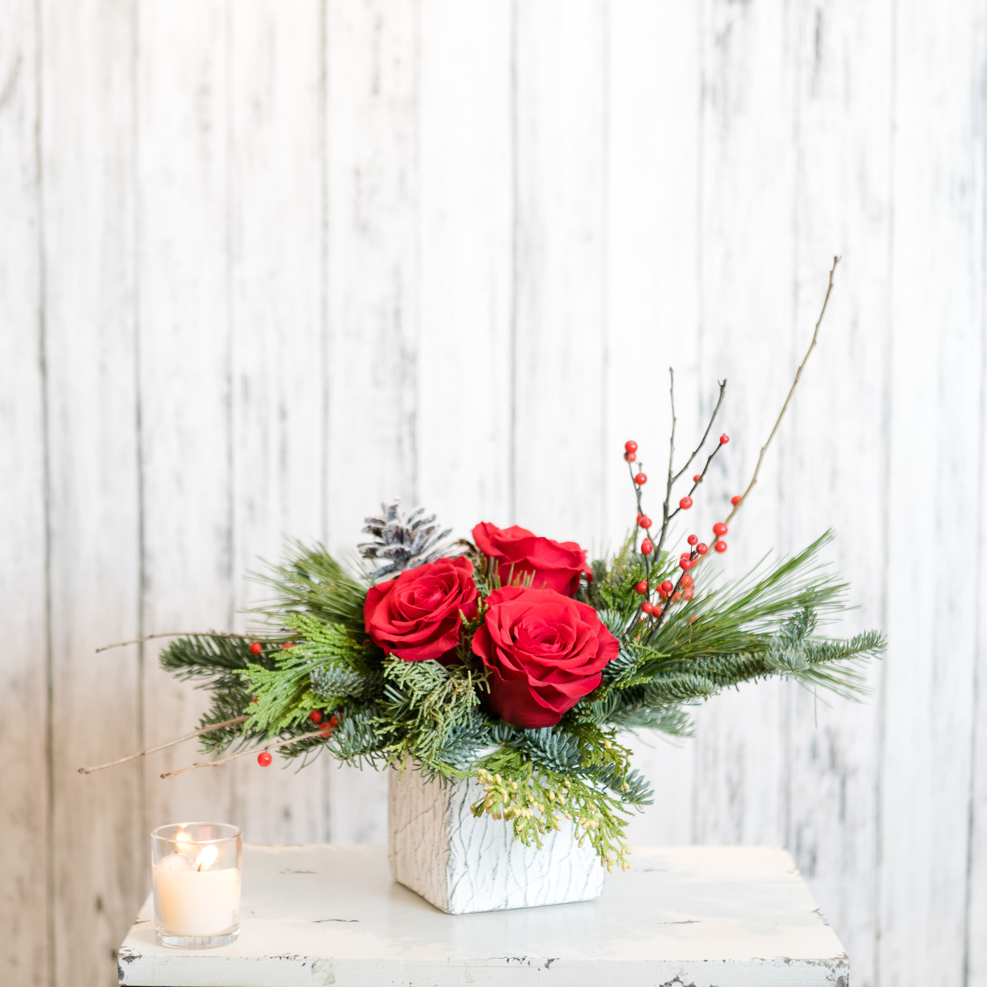Arctic - Perfect for a dining table, desk or dorm room this low profile arrangement features evergreens, winterberry and red roses in a wintery ceramic cube vase.  Approximately 16&quot; Tall X 14&quot; Wide 