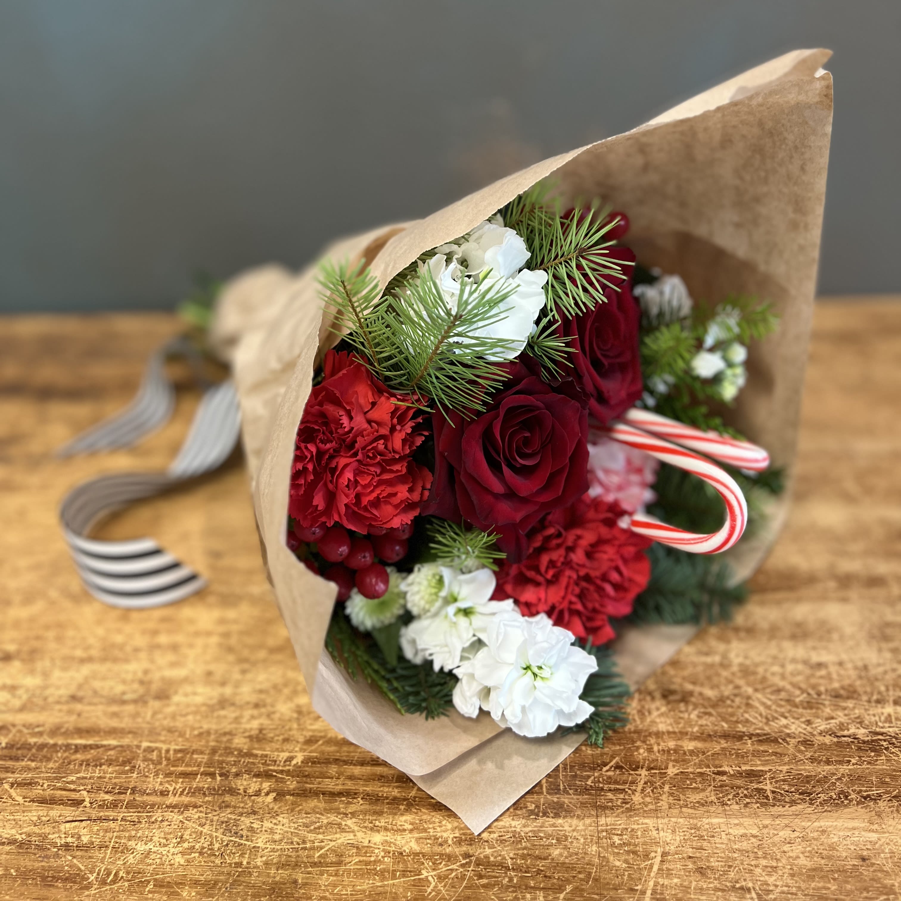Holiday Seasonal Wrap - This bouquet will make anyone's holiday season merry! Bouquet will be hand delivered and wrapped in our signature brown paper with black and white striped ribbon.