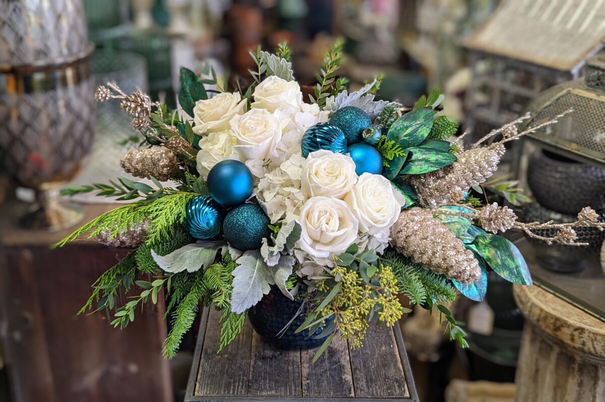 Frost - Frost – A Cool, Winter-Luxe Statement Piece Snowy, serene, and shimmering with jewel-toned magic, Frost is a winter showstopper crafted by Windmill Floral Expressions in Las Vegas. This luxurious arrangement blends lush white roses and hydrangea with icy blue ornaments, teal accents, and glistening champagne-gold botanical elements, creating a captivating balance of cool elegance and holiday sparkle.  Layered evergreen textures, frosted foliage, and shimmering cones give Frost its enchanting, winter-luxe personality—perfect for holiday tables, entryway consoles, or as a sophisticated seasonal gift. The deep teal vase adds depth and drama, anchoring the snowy palette with a rich, modern touch.  Designed for those who love bold color contrasts and wintery glamour, Frost brings an elevated, frosty-chic aesthetic to any Las Vegas or Henderson home.  SEO Keywords: