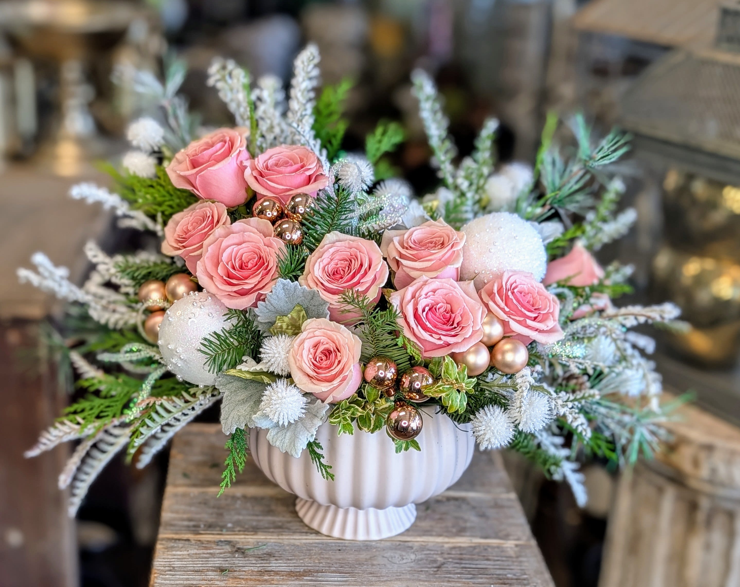 Sugar Plum - Sugar Plum – A Soft &amp; Enchanted Holiday Bloom Sweet, whimsical, and perfectly winter-dreamy, Sugar Plum is a luxe seasonal arrangement overflowing with soft pink roses, frosted textures, and delicate holiday sparkle. Created exclusively by Windmill Floral Expressions in Las Vegas, this design balances romance with festive magic—like a snowy ballet scene brought to life in flowers.  Blush ornaments, shimmering baubles, and icy white accents nestle between lush winter greenery, giving the arrangement a glistening, sugar-dusted glow. The sculpted soft-white vase adds a modern, feminine touch that pairs beautifully with mantles, holiday tables, nursery décor, or as a stunning gift for anyone who loves pastel holiday charm.  Elegant, sweet, and lightly frosted, Sugar Plum transforms any space into a soft winter wonderland.