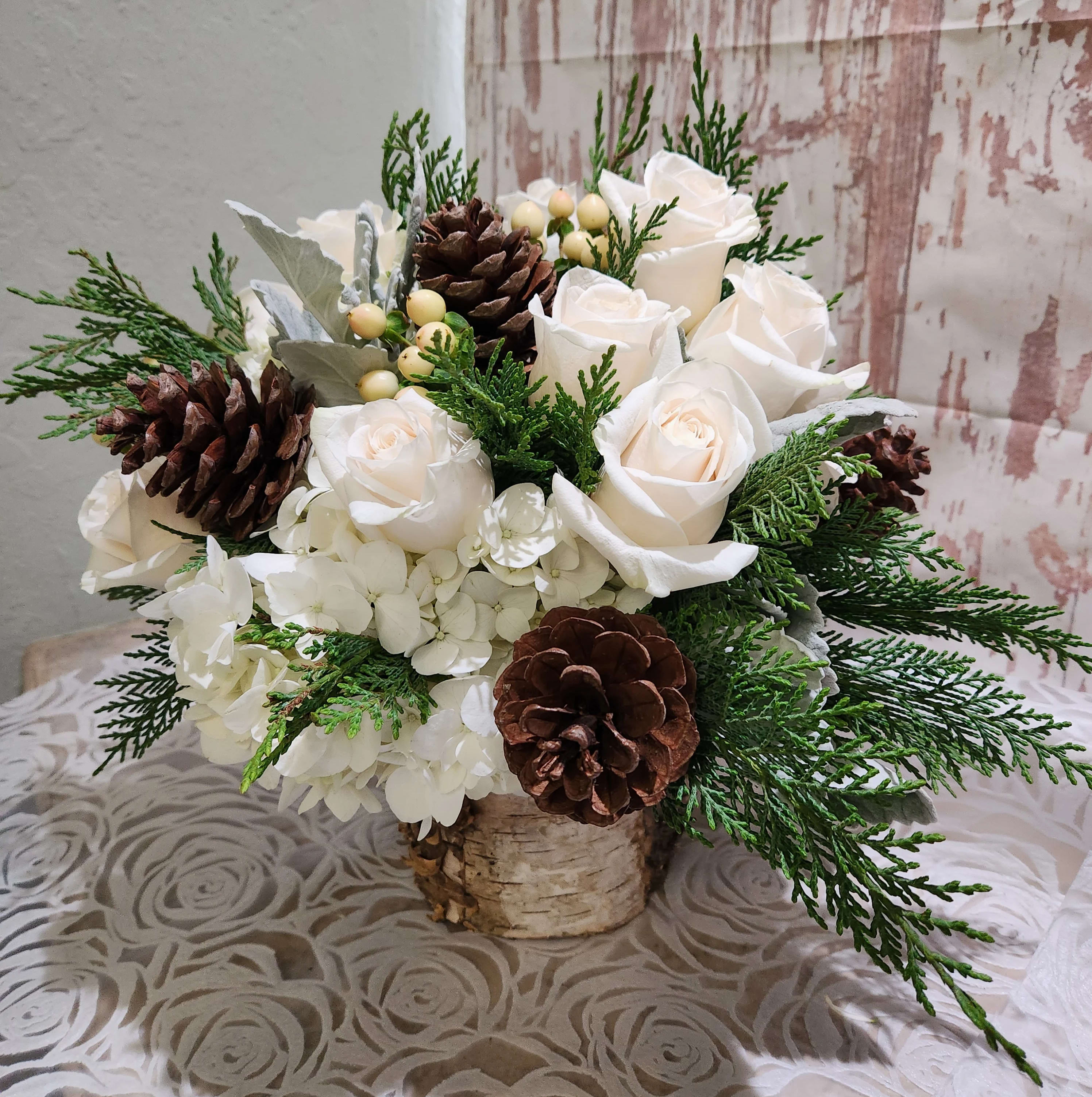 A Holiday Celebration -Birch Design Collection  - This arrangement is not only a Holiday celebrations it's an all month celebration kind of gift.  A gorgeous mix of white creamy roses, white lush hydrangeas , dusty miller and green berry's and more accented with cedars evergreens. Designed in a beautiful glass vase lined with a birch ribbon liner.  Cube or cylinder style vase . Containers may vary depending on inventory. Standard will have 5 roses  Deluxe- 7 roses  Premium - 10 roses        