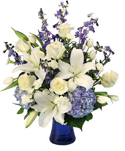 ELEGANCE OF WINTER - This gorgeous beauty is perfect for the season! The white roses, tulips, lilies, and mini carnations stand out against the beautiful blue delphinium and hydrangeas, making Elegance of Winter a spectacular season classic. With elegant whites and pops of blue, this design is sure to be a stunning gift!