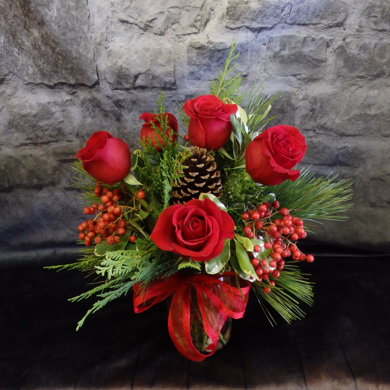 Berry Merry - Festive, Elegant and Fun for this arrangement. Christmas greenery, berries and 6 Red roses displayed in a glass jar and tied with pretty red ribbon.  H01-17 