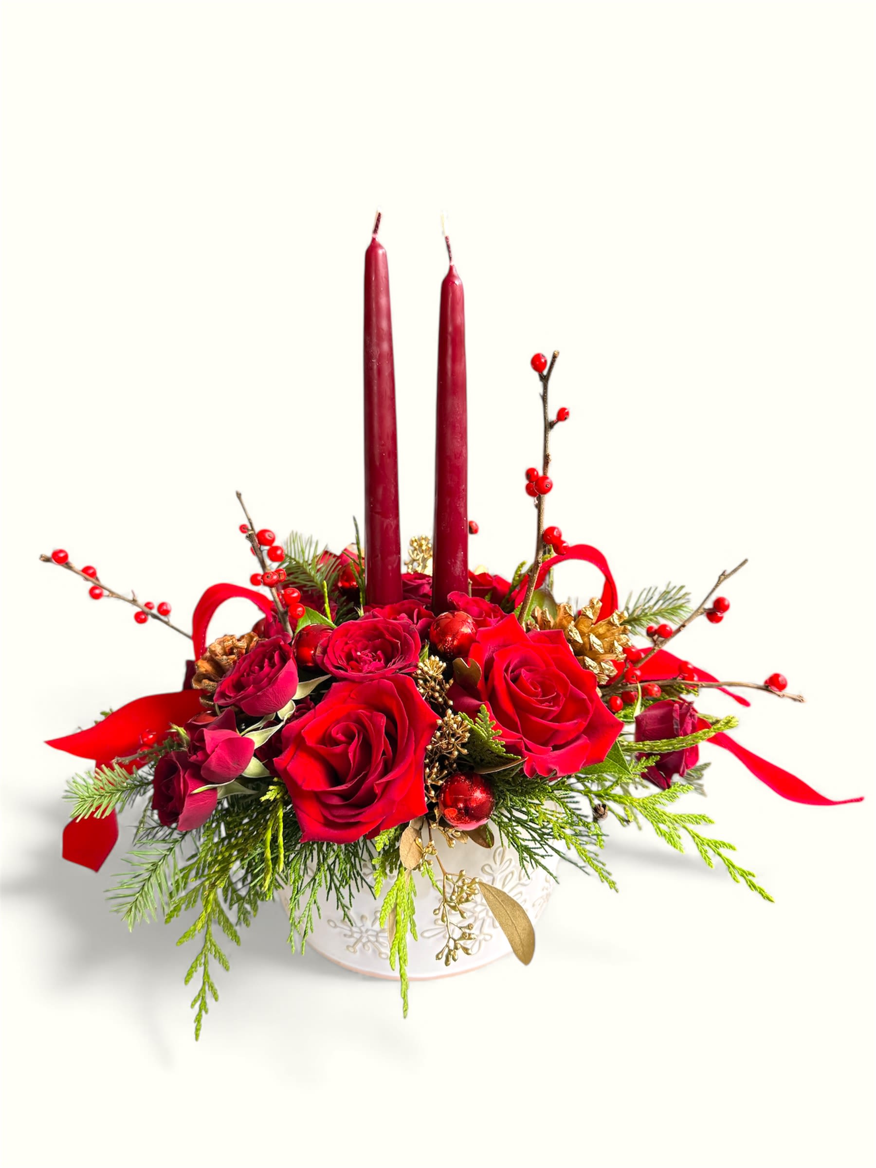 Snowflake Sparkle Centerpiece - Make your holiday table unforgettable with this stunning Snowflake Sparkle centerpiece. Rich red roses, festive berries, lush evergreens, and shimmering gold accents are beautifully arranged in an embossed cream ceramic bowl. Finished with two deep red taper candles and holiday ribbon, this design brings warmth, elegance, and classic Christmas charm to any celebration.