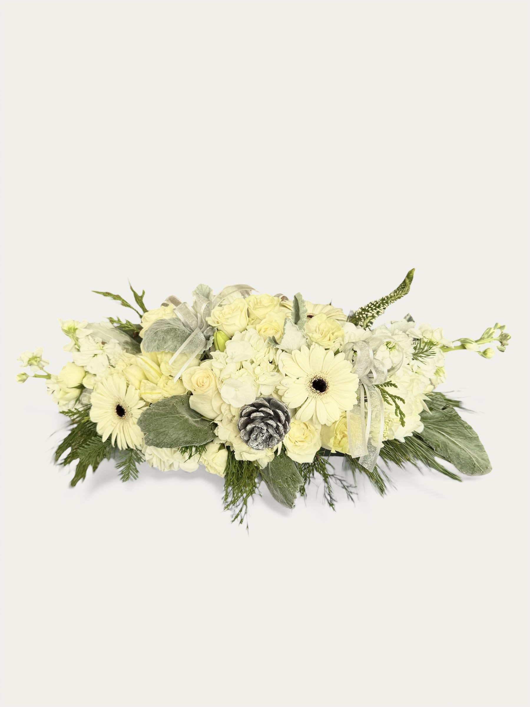 Winter Rose Centerpiece - Our Winter Rose centerpiece floral arrangement features a luxurious blend of creamy white roses, gerberas, and seasonal booms, beautifully accented with frosted greenery and a silver tipped pinecone for a subtle winter touch. Soft textures and cool tones create a serene, snow-inspired aesthetic perfect for holiday tablescapes.