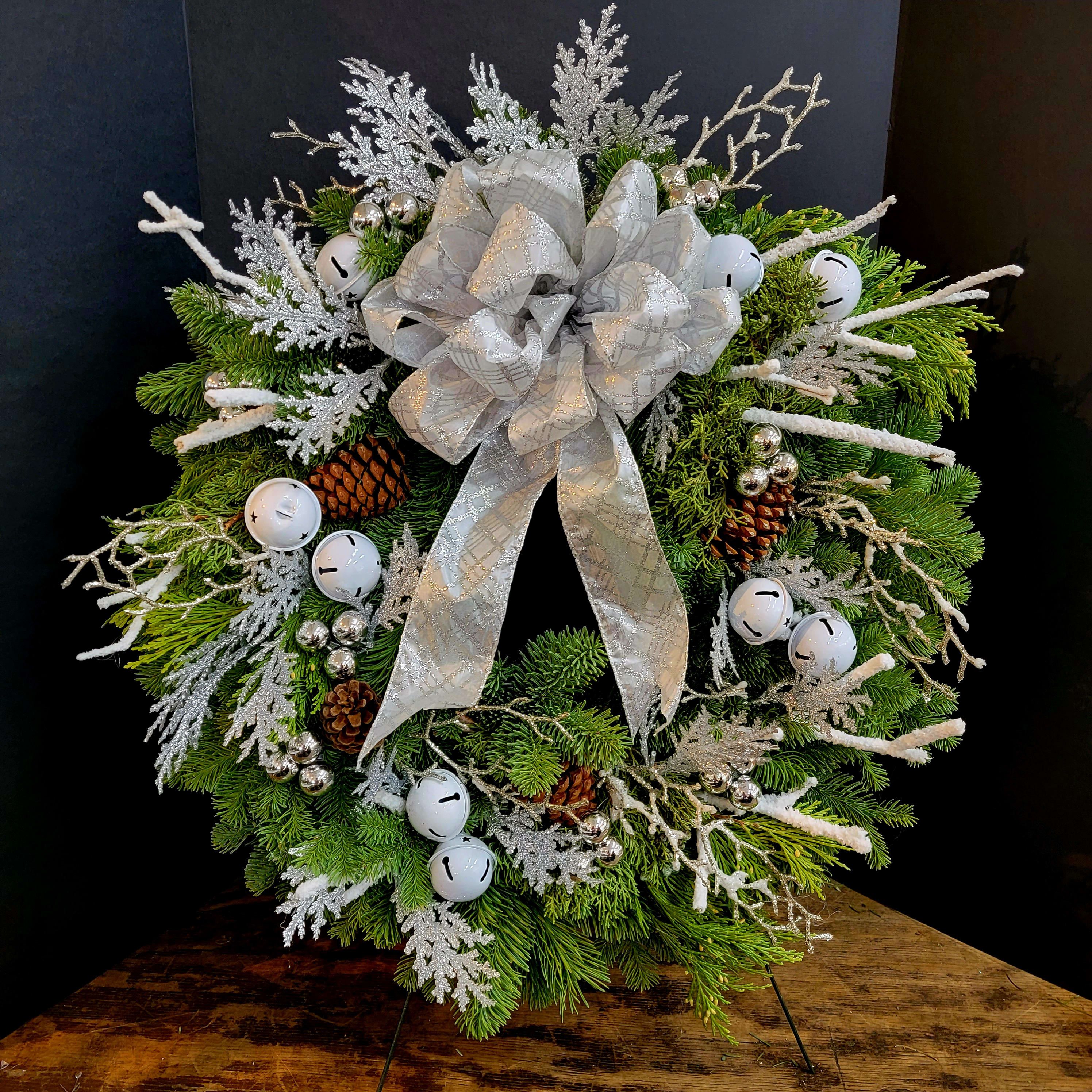 Silver Splendor  Holiday Wreath - When it comes to saying &quot;Merry Christmas,&quot; this wreath offers a silver opportunity to say it in style! An elegant noble fir wreath is adorned with a beautiful silver bow, white jingle bells, silver ornaments, pinecones and more. Perfect for your own house, or the home of a loved one. In this case, all that glitters really is silver! Approximately 30&quot; W x 30&quot; H