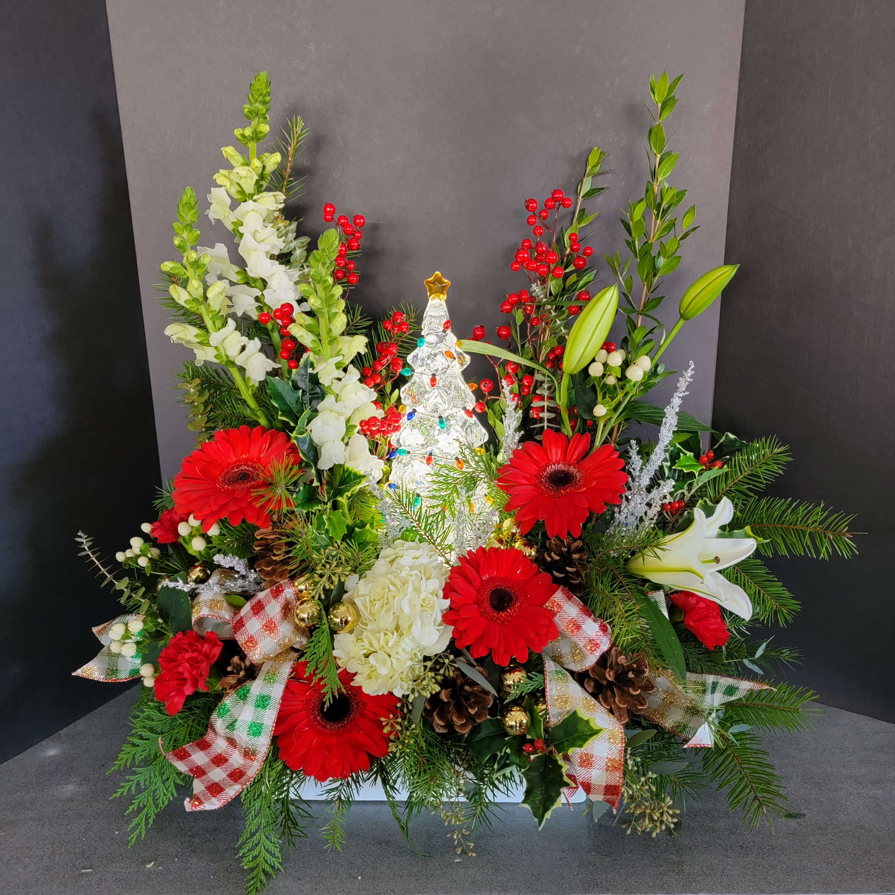 Winter Wonderland with Light-up Tree - Send a Christmas bouquet they'll adore for many years to come! This light-up collectible tree makes for a beautiful gift and features sweet holiday flowers made up of roses and winter greens. Red gerbera daisies, white lilies, white snapdragons, red carnations red and white berries, pine cones &amp; ribbon loops  are arranged with noble fir, cedar, white pine, seeded eucalyptus and dusty miller. Delivered with a battery powered (included) beautiful light-up tree. Orientation: All-Around