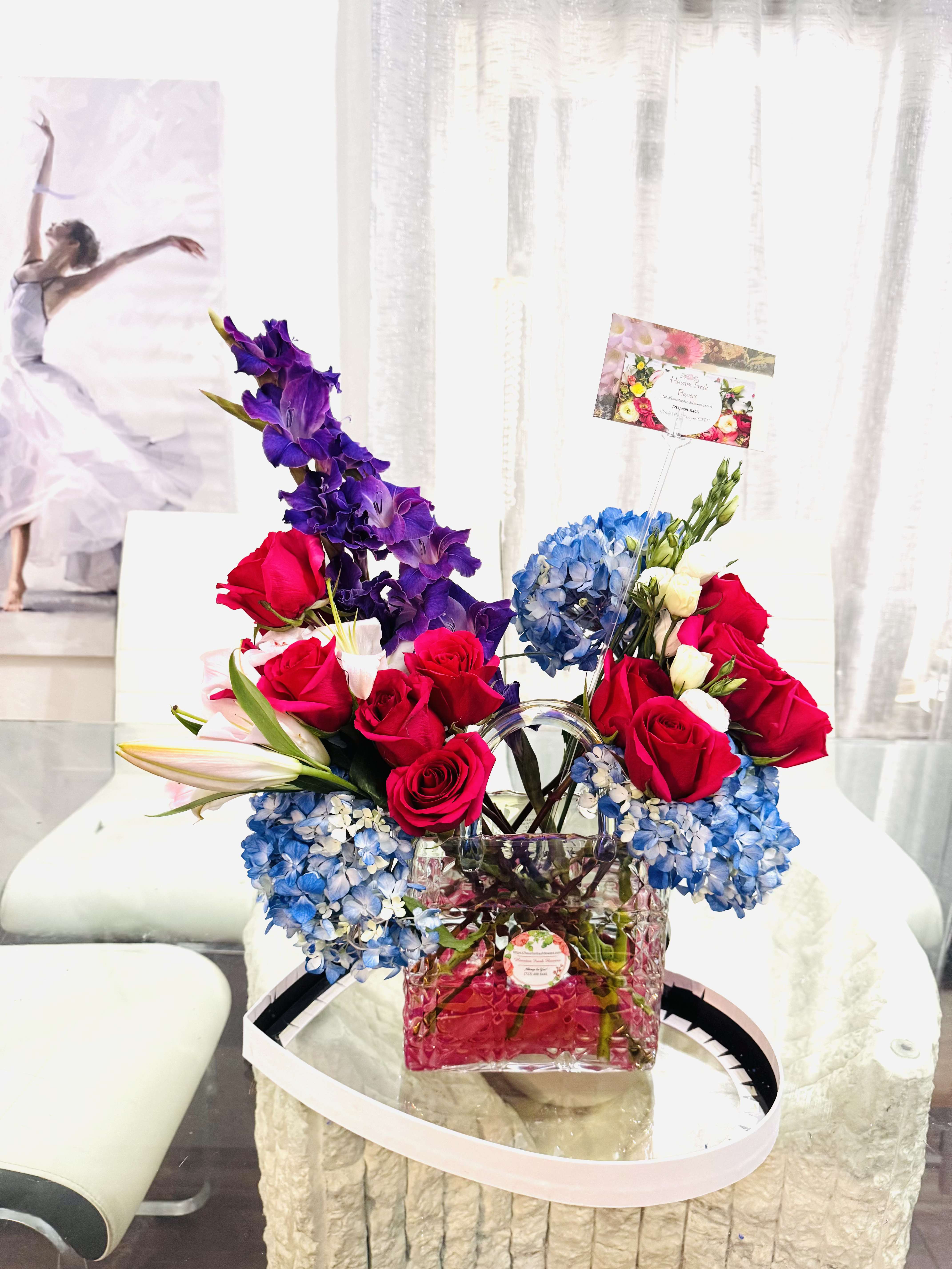 Designer's Choice pre-order ahead - This Flower arrangement has a striking, almost theatrical elegance. With modern glass vase, lined with red stones, bursts forth a vibrant harmony of colors. Red roses (please give a call if you need different color) take center stage, symbolizing passion and romance. They are complemented by clouds of blue hydrangeas, adding depth and softness, like fragrance of summer skies. This is not just a bouquet, but a statement piece: Modern Romance captured in flowers, perfect for a grand gesture or a sophisticated celebration. 