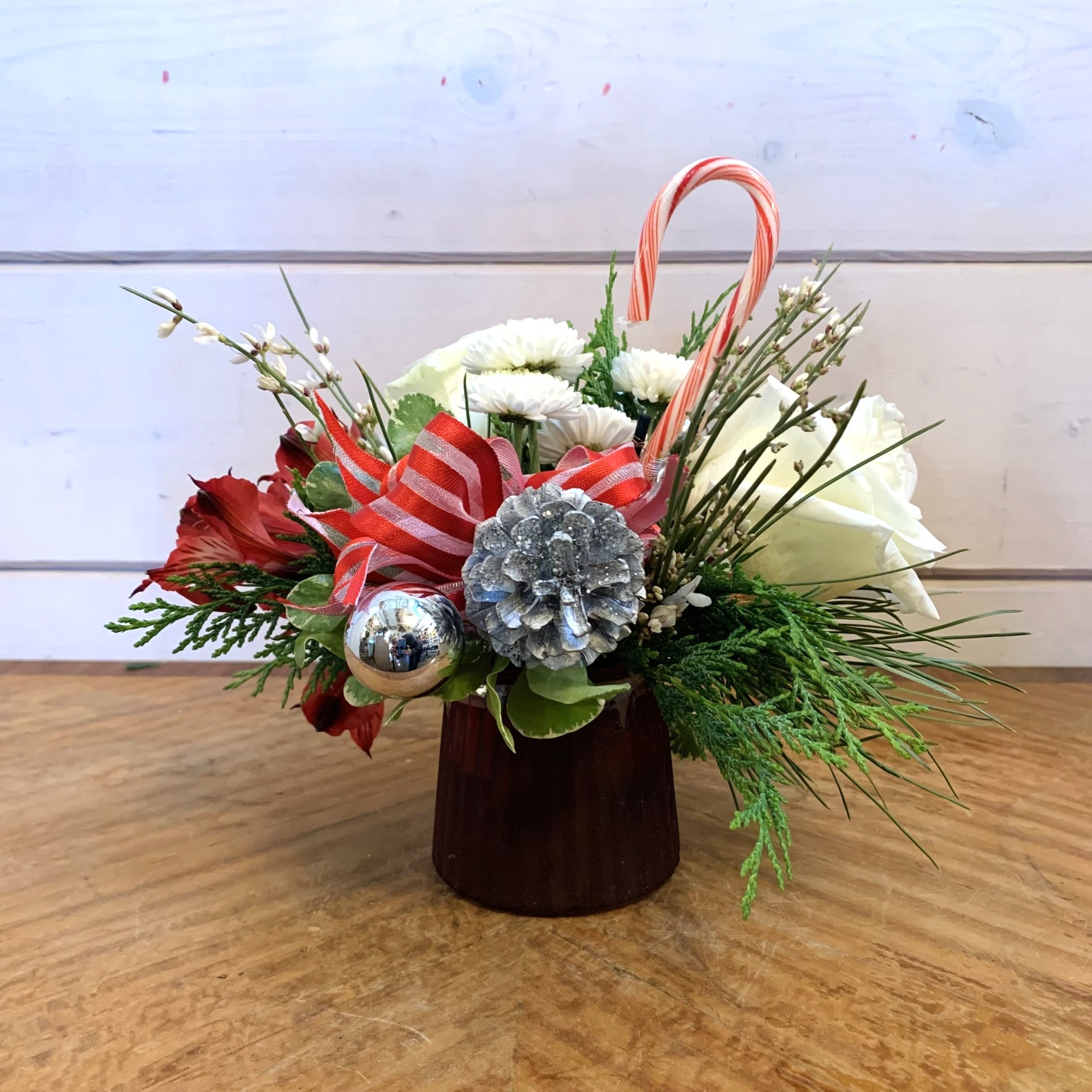 A Little Peppermint - This petite red and white arrangement matches its candy cane insert with white roses, white button chrysanthemums and red alstroemeria in a petite burgundy glass with white seasonal filler flower, a red striped bow and silver accoutrements. Approximately 6&quot; tall and 6&quot; wide.