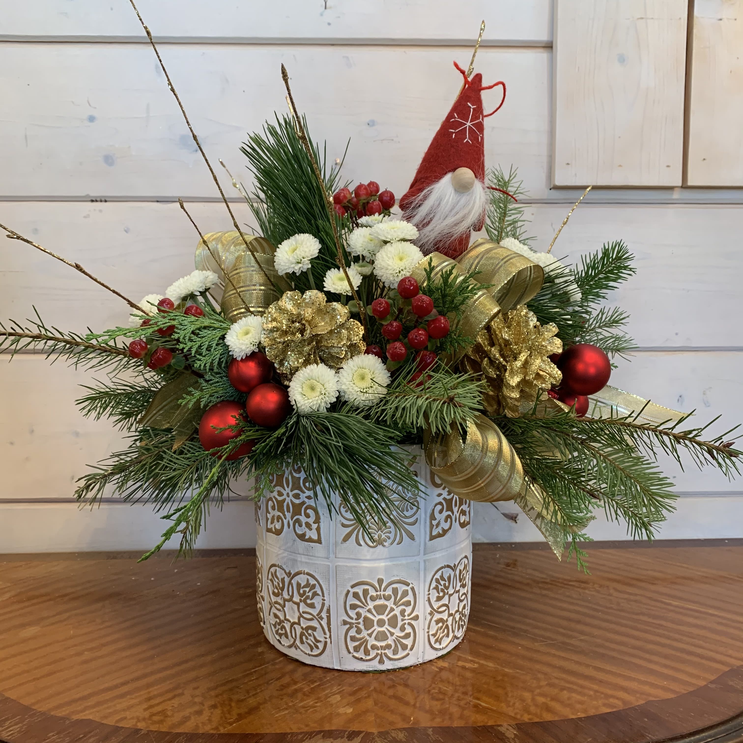 Delight of December  - This long lasting arrangement is made with red hypericum, white buttons, large gold bows, gold pine cones and red ornament balls styled in an extra large white and gold vase with gold glitter branches and a festive Swedish gnome. Approximately 18in tall and 18in wide.  