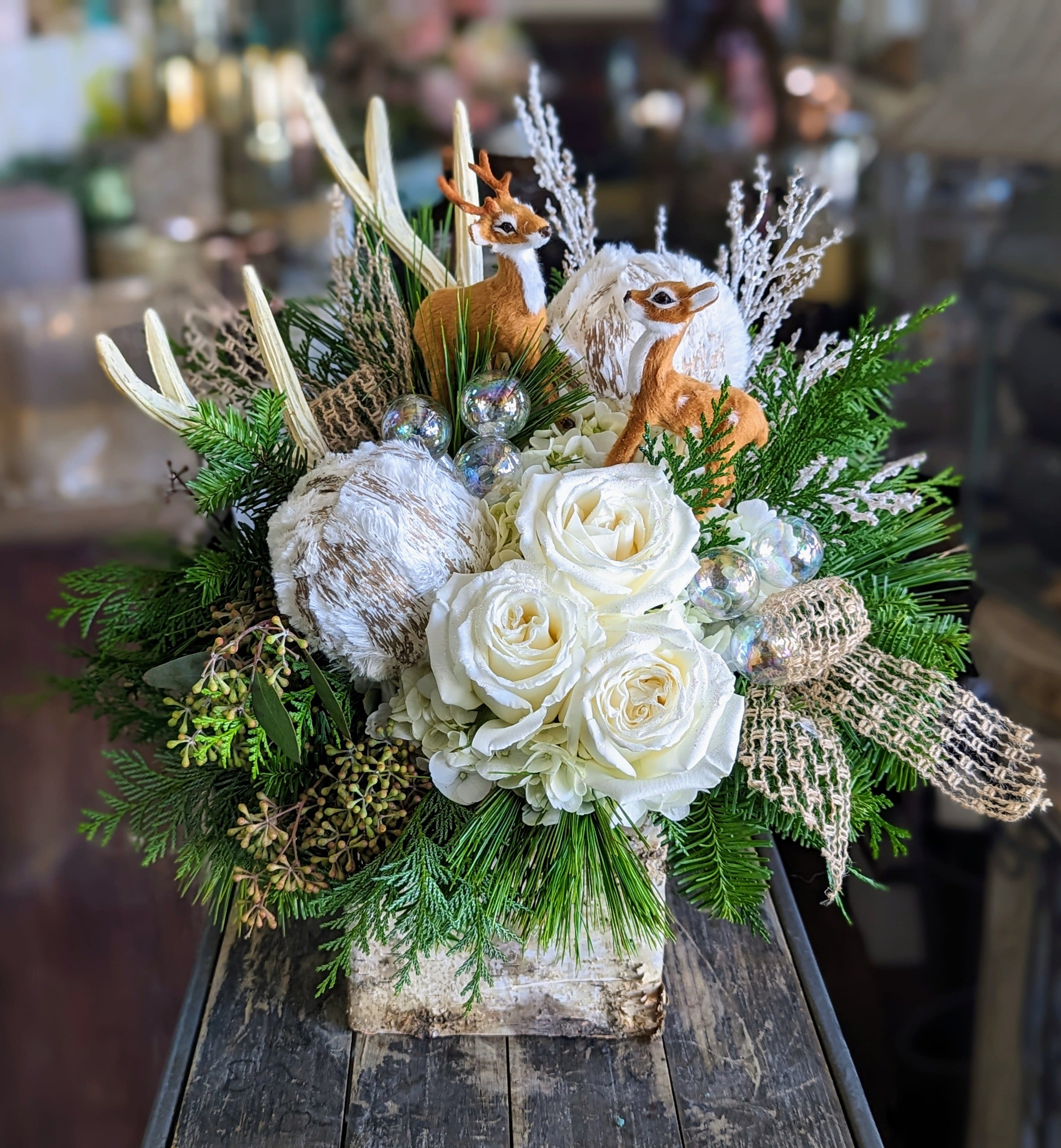 Oliver and Rose - Oliver &amp; Rose – A Woodland Winter Story Charming, cozy, and full of woodland magic, Oliver &amp; Rose is a whimsical holiday arrangement designed by Windmill Floral Expressions in Las Vegas. This enchanting piece blends creamy white roses and hydrangea with lush winter greenery, frosted botanical textures, and iridescent ornaments that sparkle like freshly fallen snow.  Nestled among the blooms are two adorable woodland deer—Oliver and Rose—bringing personality and storytelling to the arrangement. Soft, snow-dusted pods, rustic burlap ribbon, and natural pine elements enhance the forest-inspired aesthetic, creating a warm and inviting winter scene in floral form.  Perfect for holiday mantles, woodland-themed décor, children’s rooms, or gifting to someone who loves nature with a touch of whimsy, Oliver &amp; Rose brings a serene, storybook charm to any Las Vegas or Henderson home.  SEO Keywords: