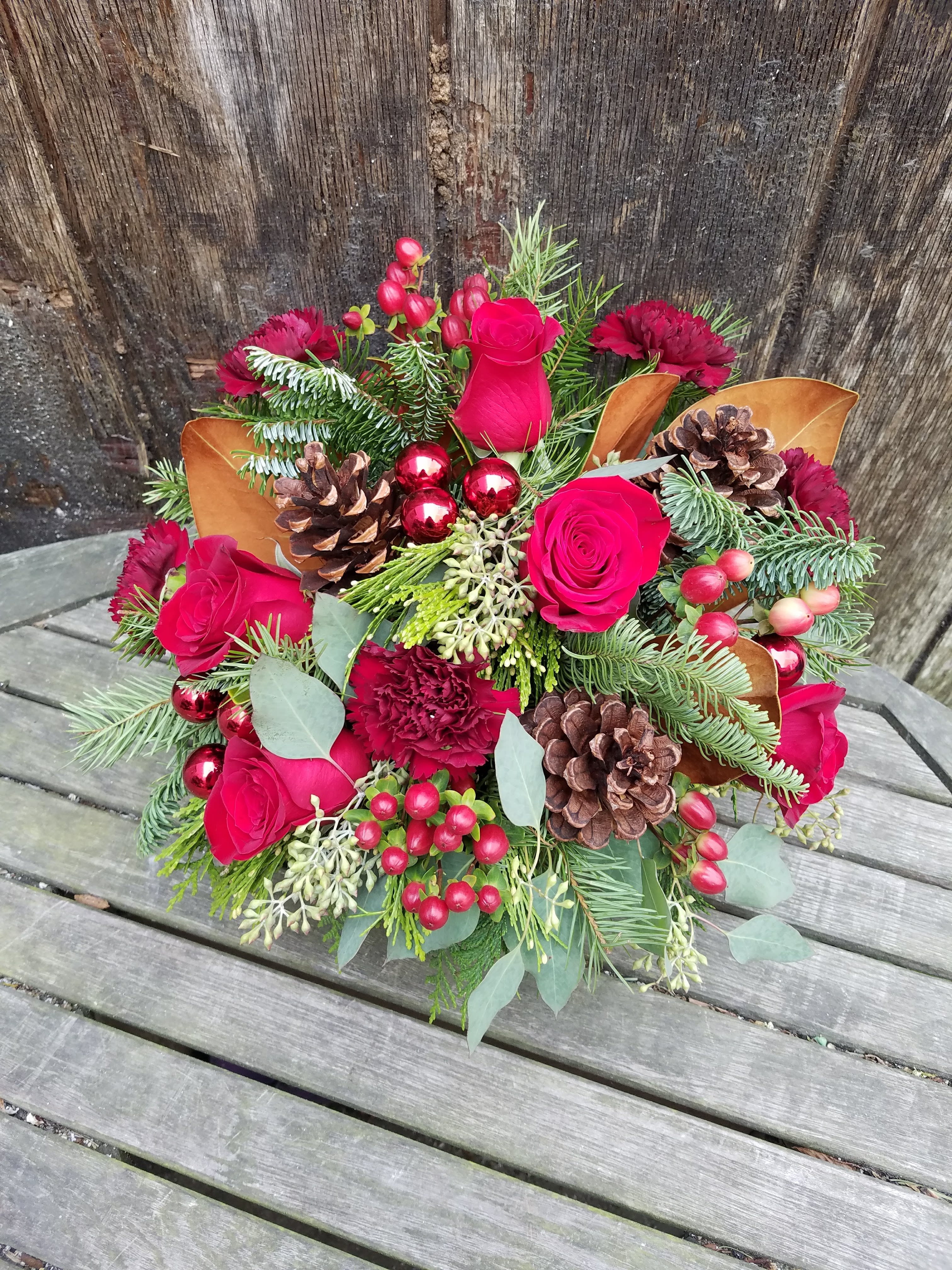 Winter red arrangement - LUX CHRISTMAS FLOWERS WITH RED ROSES &amp; CARNATIONS  Warm and bright. This glorious vase of Christmas flowers is the perfect gift for loved ones to celebrate the holiday season. Ruby red roses blend beautifully with chocolate-colored magnolia leaves and rustic pinecones. While rich burgundy carnations and dainty red berries add lashings of luxury. Classic evergreen will bring a fresh fragrance into the home and the design’s shiny red ornaments create an instant festive vibe.  Why not add a greeting card or quality handmade candle as an extra thoughtful touch to your Christmas gift?  Winter Red Arrangement features: -Velvety red roses -Dainty red hypericum berries -Frilly burgundy carnations -Noble fir -Fragrant cedar -Seeded eucalyptus -Magnolia leaves -Decorative pinecones -Shiny red ornaments -Clear glass vase  SIZE: The STANDARD flower arrangement is approximately 8” height and 9” width.  ALLERGY ADVICE: This design has low pollen and a low-moderate fragrance.     Ready to bring floral beauty into someone’s world with these beautiful Christmas flowers? Order this gift online now or give us a call on (415) 752-2060 if you have a question or special request.  