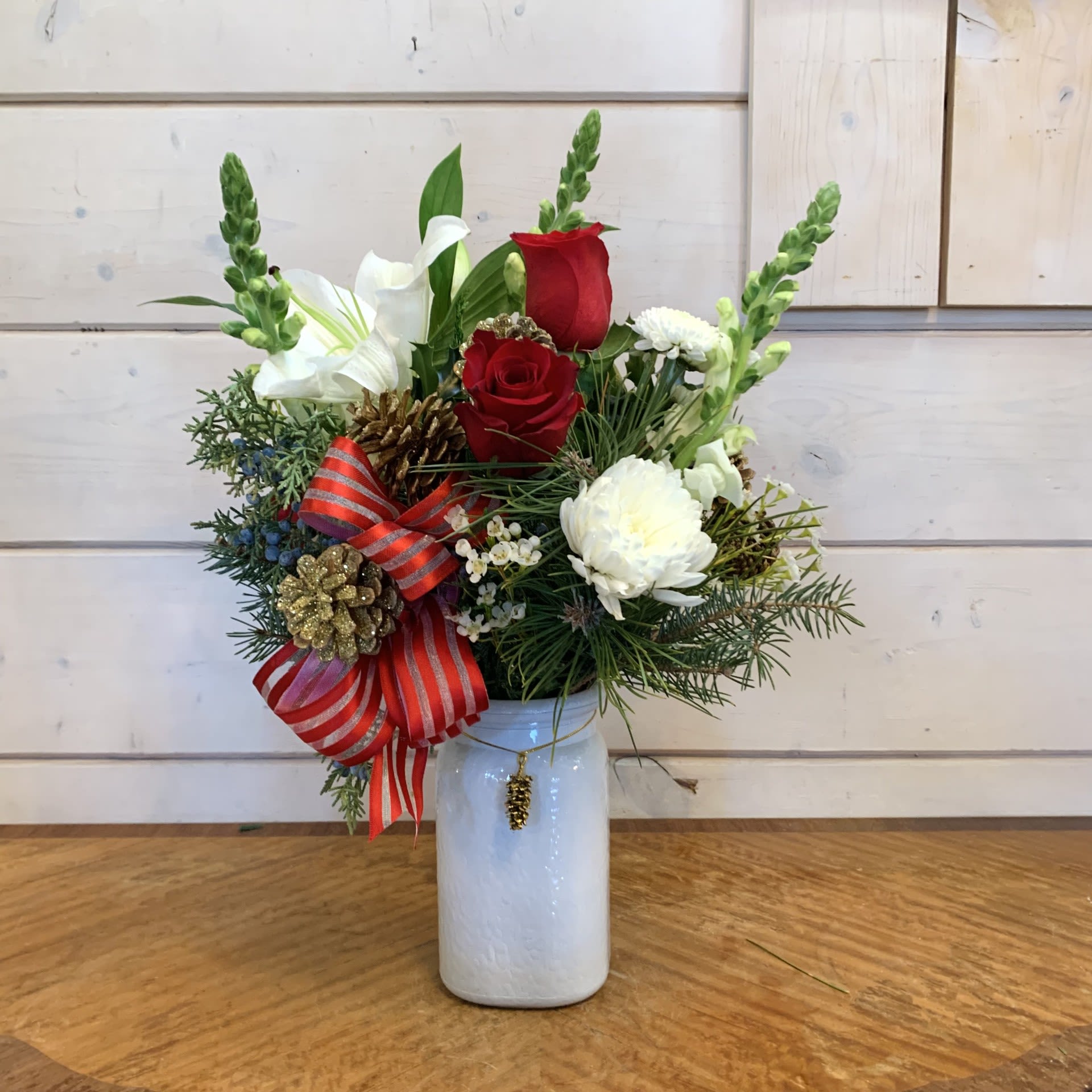 O' Holy Night - This classic red, white and gold christmas arrangement features red roses and white lilies with white chrysanthemums, a red striped bow, and gold pinecones in a white mason style vase with a gold pinecone charm. Approximately 14" tall and 10" wide.