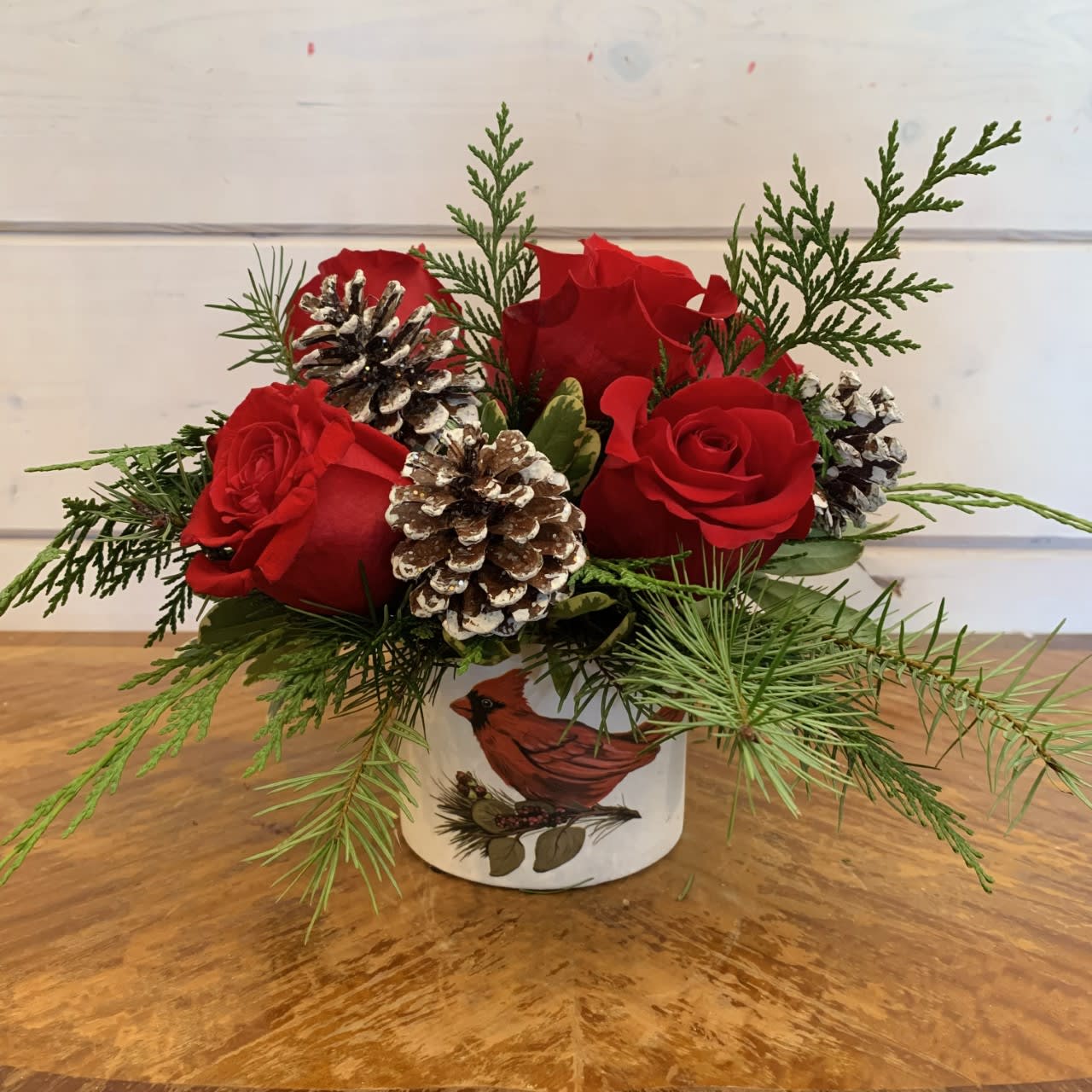 Pinecones and Roses Bouquet  - This sweet arrangement is made with 6 red roses and 6 frosted glitter pinecones arranged in a small red cardinal ceramic pot. Approximately 8in tall and 9in wide. 