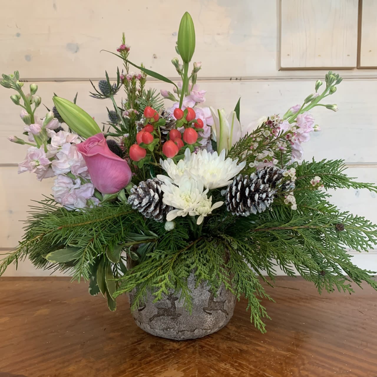 Pink Holiday Bouquet  - Pink roses, stock and hypericum berries are mixed with stargazer lilies, blue thistle and which chrysanthemums in a medium cement pot embossed with reindeer and snowflakes. Includes seasonal winter evergreens and snowy glitter pinecones. approximately 12in tall and 12in wide.  
