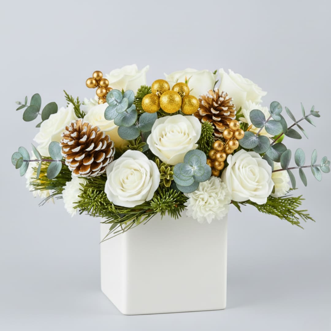 Winter's Golden Glow - "Winter's Golden Glow" is a lush, sophisticated holiday design featuring pristine white roses and fresh winter greenery, including pine and blue-toned Eucalyptus. The arrangement is richly accented with natural, snow-tipped pinecones and clusters of brilliant golden berries and ornaments. Presented in a modern white square vase, this arrangement captures the elegance and sparkle of a classic winter holiday.