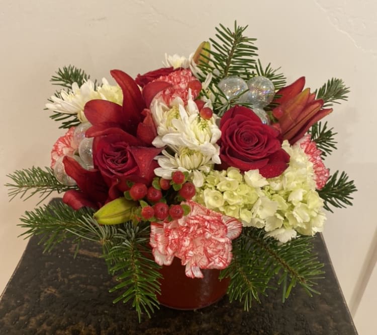 Home for the Holidays - A classic Christmas arrangement designed in a red cylinder vase. Filled with fresh flowers in reds and white. Finished off with fresh evergreens (yummy smells) and ball ornaments. 