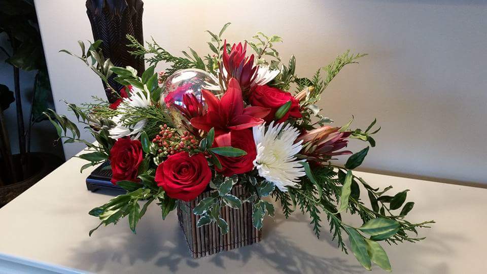 Rustic Christmas - A rustic wooden box filled with fragrant, flowing Christmas greens, fresh roses, lilies, and berries in hues of red with a pop of white chrysanthemum. Finished with a glass ornament. 