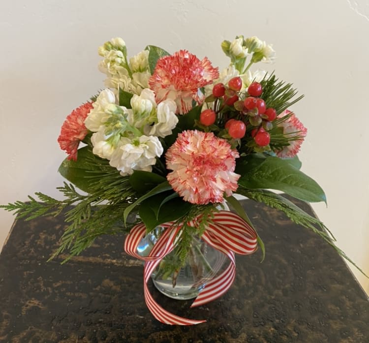 Santa's Helper - A sweet holiday design of peppermint carns, red roses, white stock, red hypericum berries and fresh evergreens. Designed in a clear glass vase. Finished off with festive striped ribbon. 