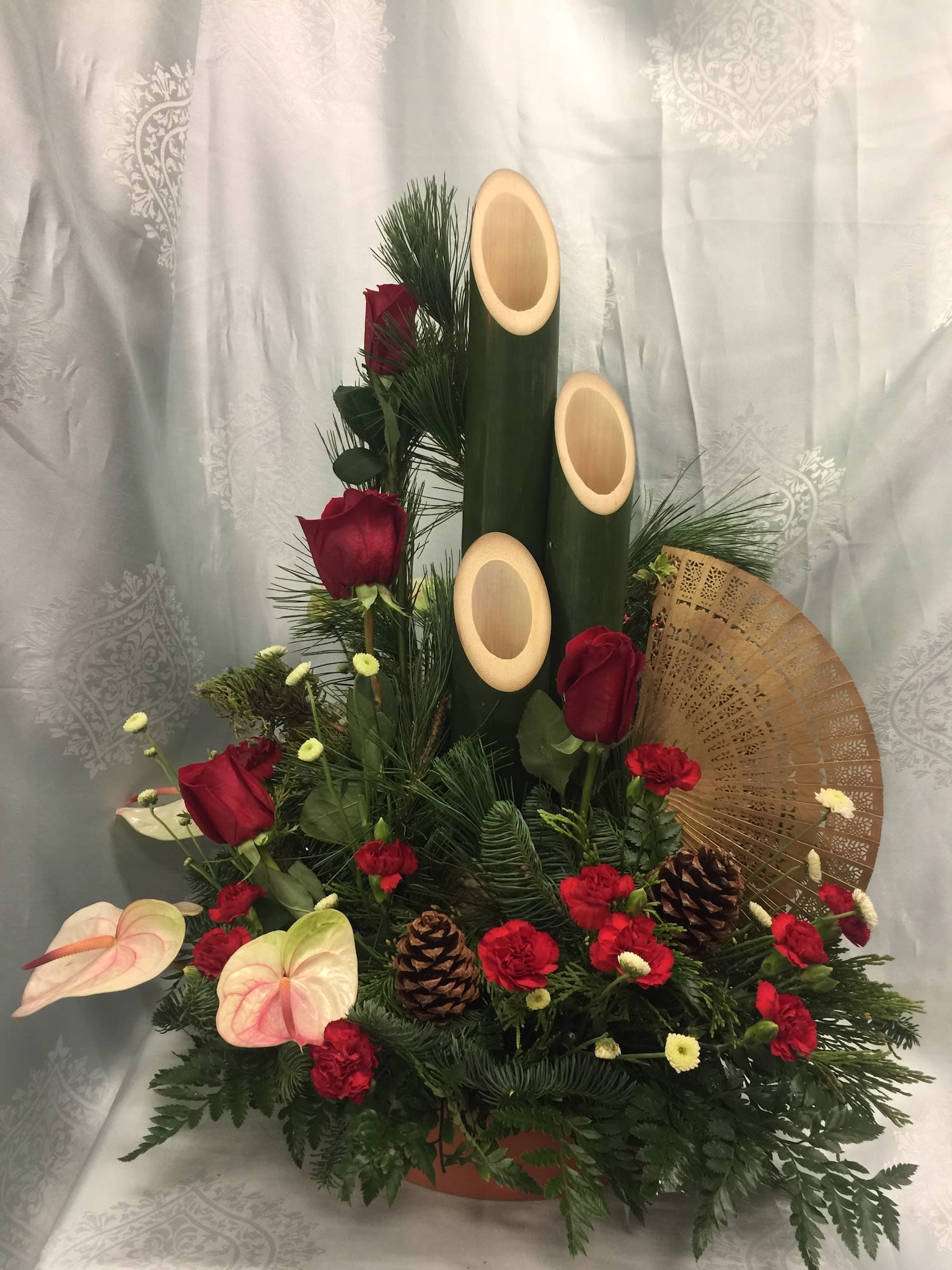 Red roses &amp; antherium Kadomatsu with fan - Elegant &amp; sophisticated red roses uplifted by antherium and stately Kadomatsu bamboo. Oriental fan and winter green and pine cones add to the overall elegant statement 